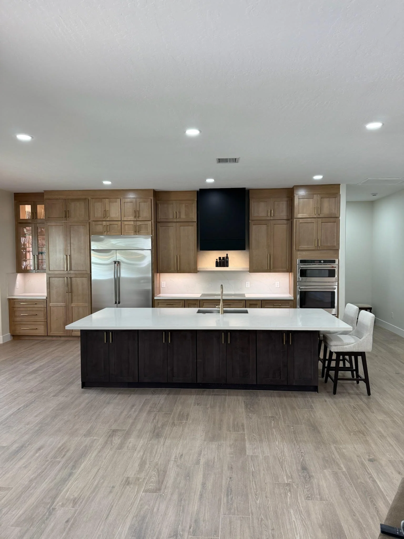 Modern kitchen with wooden cabinets, a white island with dark lower cabinets, stainless steel refrigerator and double oven, and a black range hood.