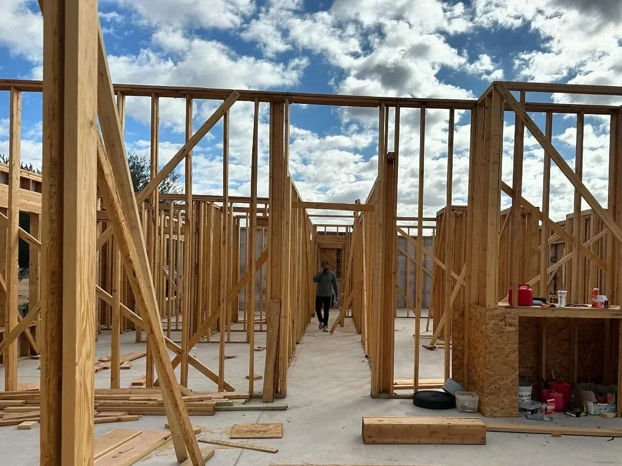 Wooden framing of a building under construction with a man walking in the middle, partly cloudy sky above.