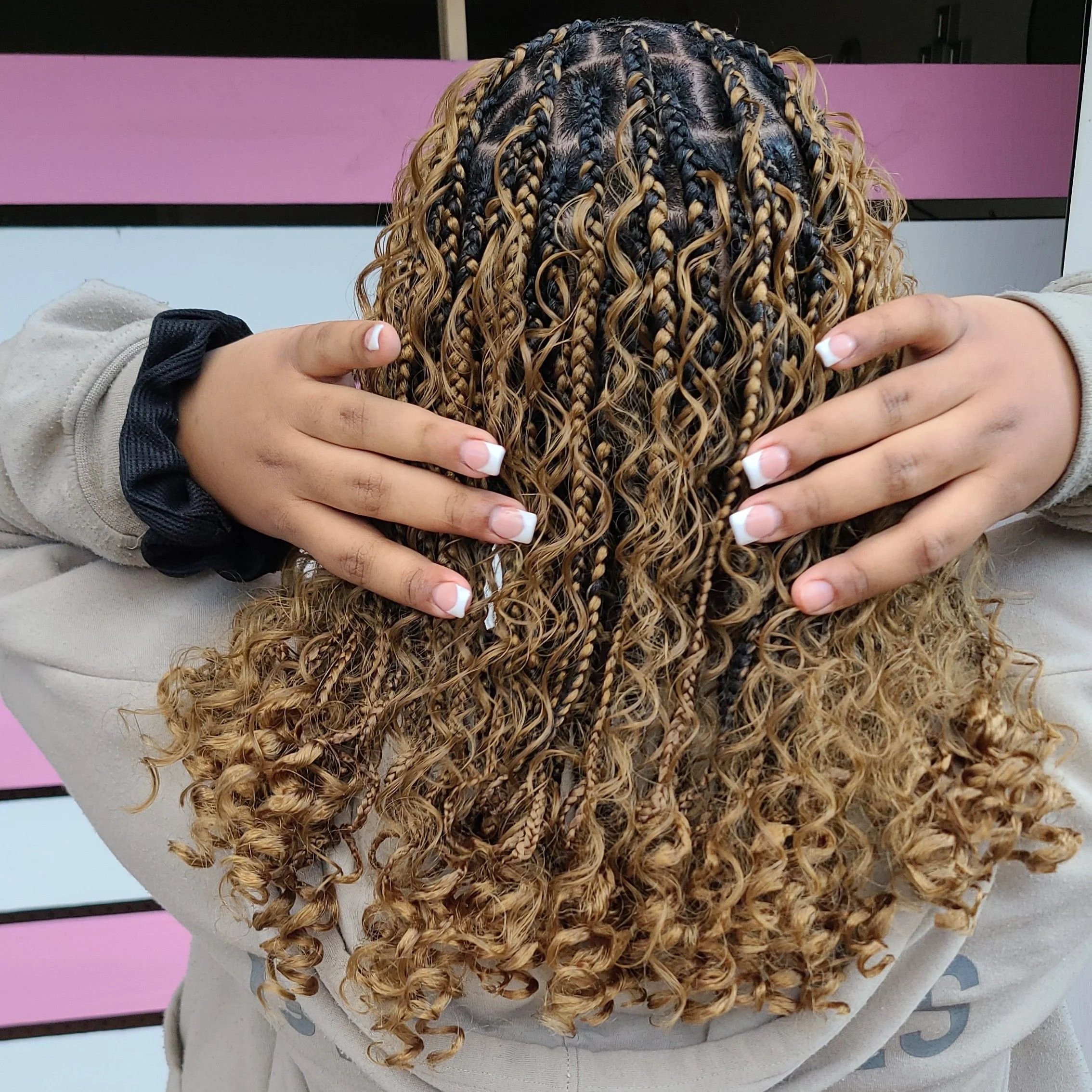 Person with curly blonde hair holding their head, showing the back of their head with braided and curled hair.