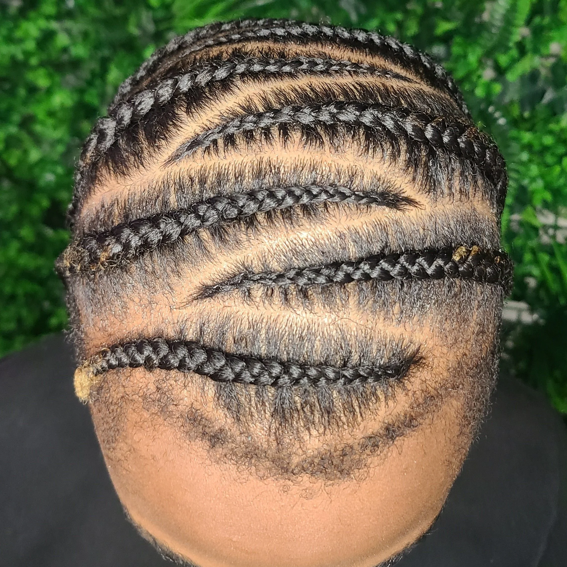 Top view of a person's head with meticulously styled cornrow braids against a blurred green background.