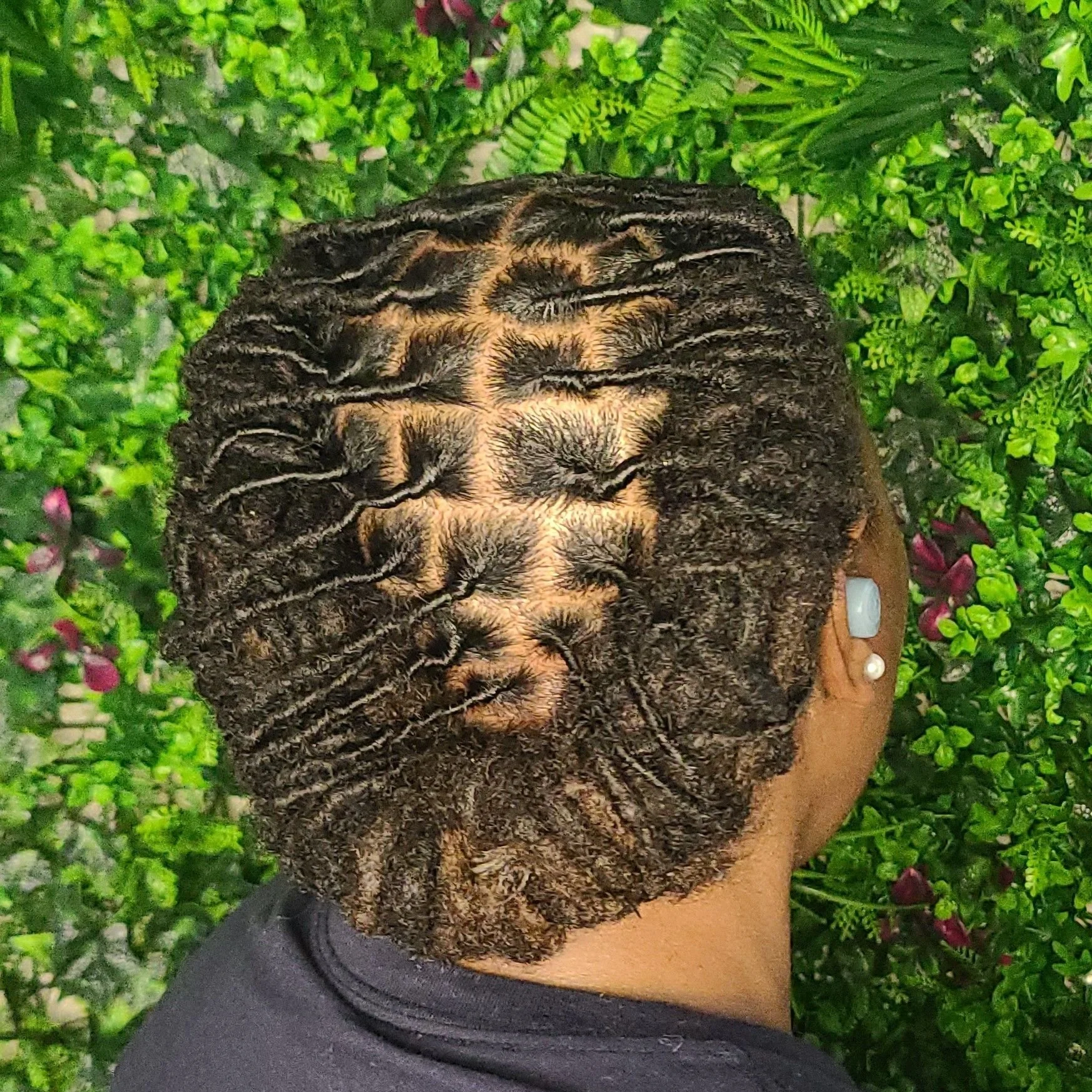 A close-up of a person's head showcasing beautifully styled dreadlocks, back of head, with green foliage in the background.