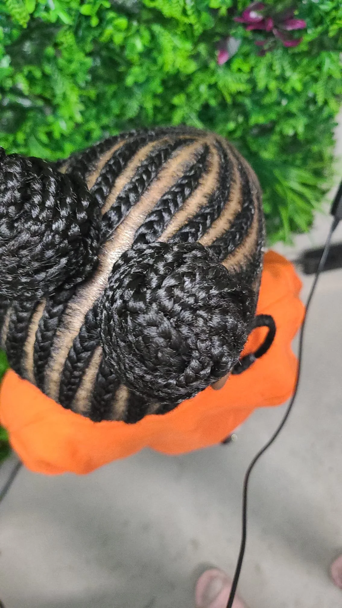 Top view of a person's head showcasing intricately styled braids with a mix of black and beige colors, resting on an orange surface.