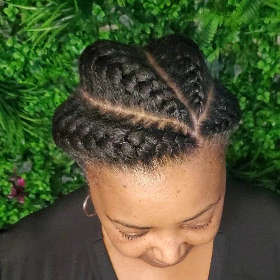 Top view of a woman with braided hairstyle and a center part, surrounded by green foliage.