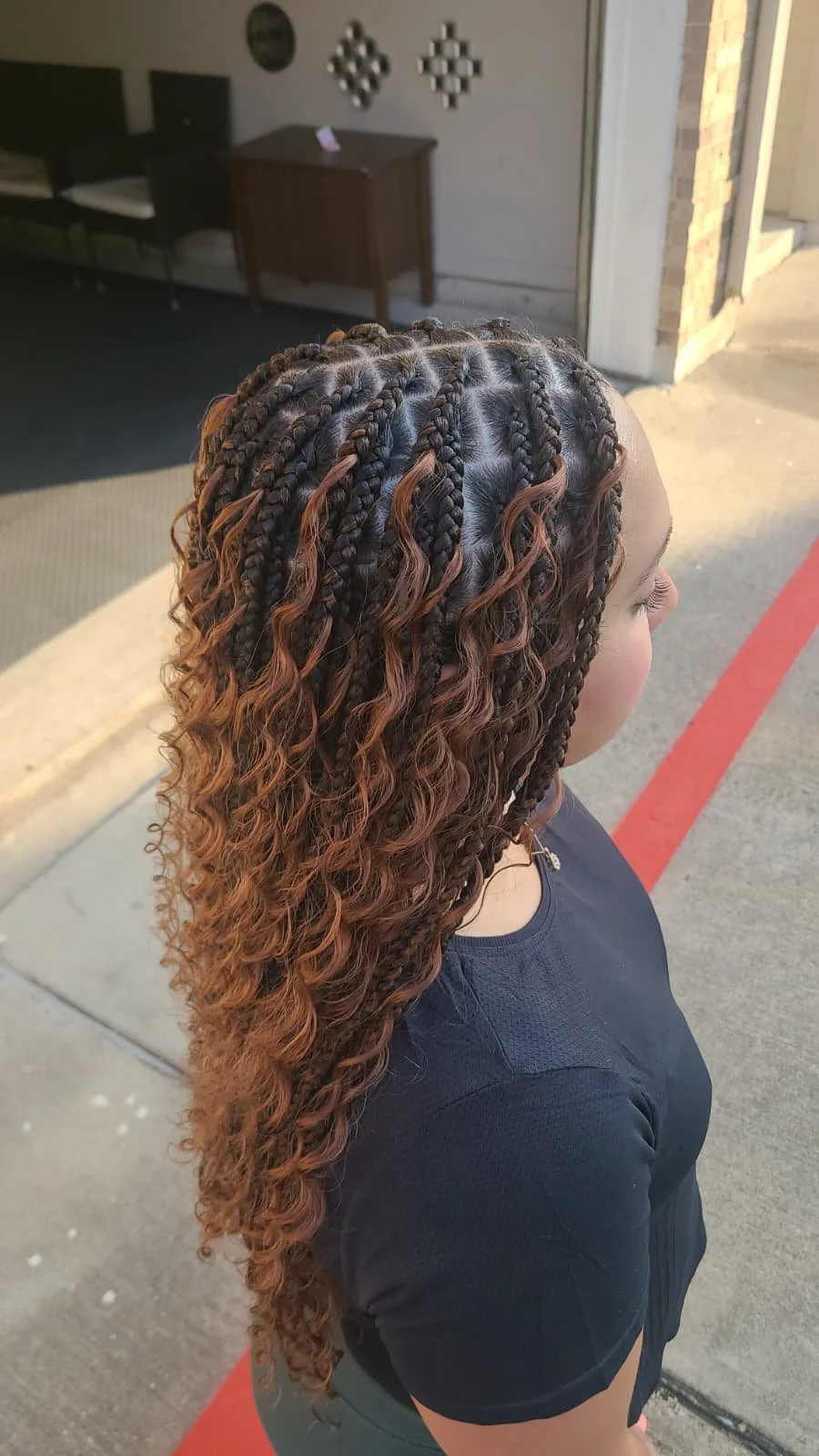 Side view of a young woman with curly, braided and ombre hair, standing outside near a building entrance.