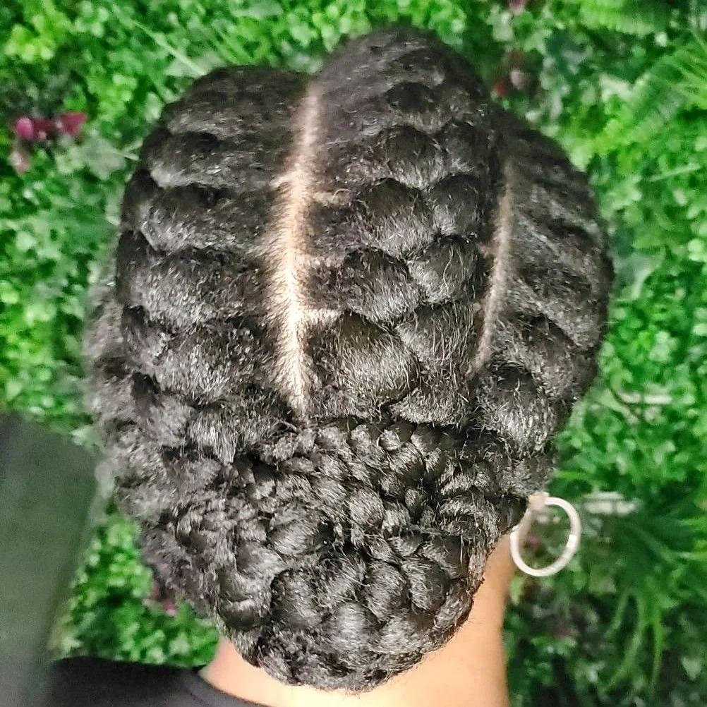 Close-up view of a person's head showing intricately styled, tightly coiled black hair with a prominent middle part.
