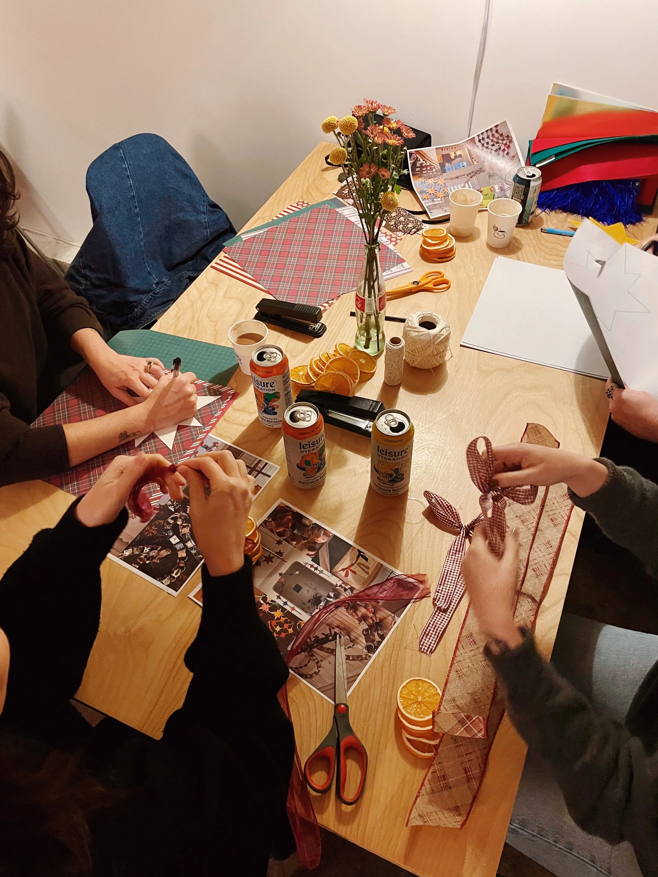 People preparing for a craft or gift wrapping activity, with scissors, ribbons, photos, and holiday decorations on a wooden table.