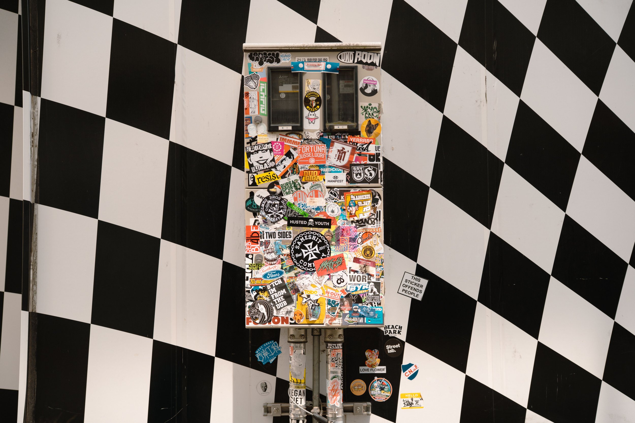 A parking meter covered in various colorful stickers, set against a black and white checkered background.