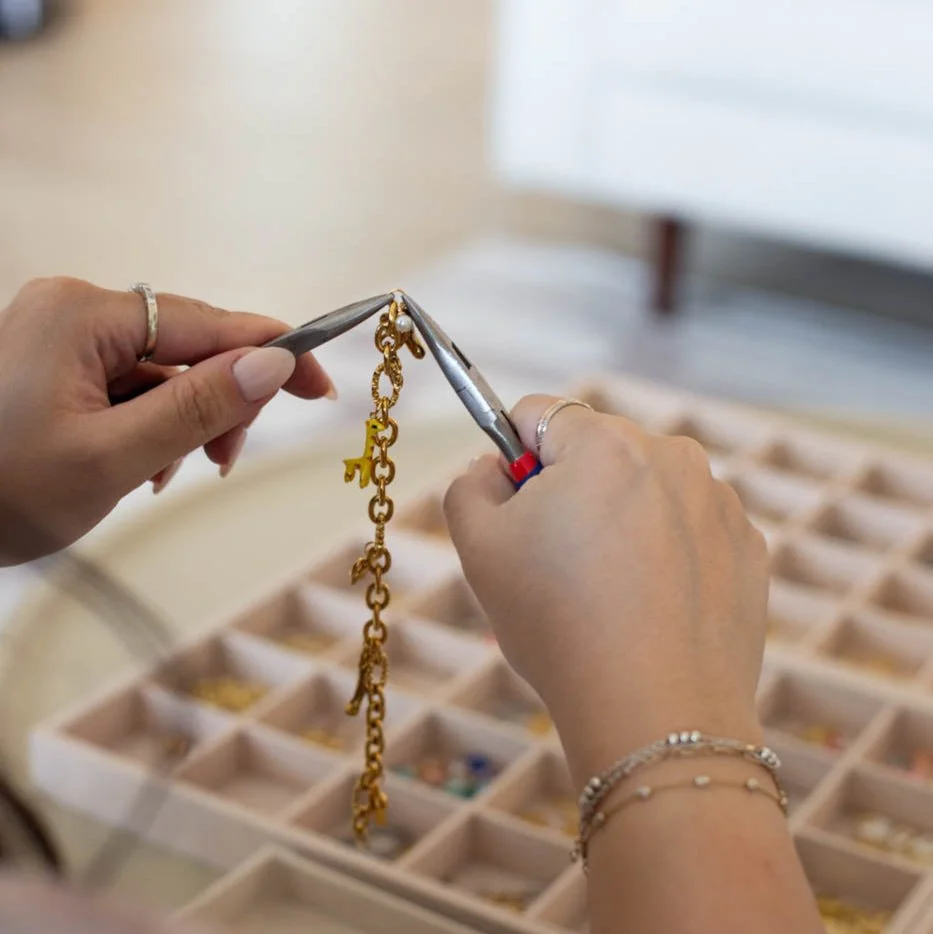 A decorative jewelry box with gold accents, shaped like a heart, is placed on an open sheet of music surrounded by pink and white peony flowers, a string of pearls, earrings, and a small pink perfume bottle.