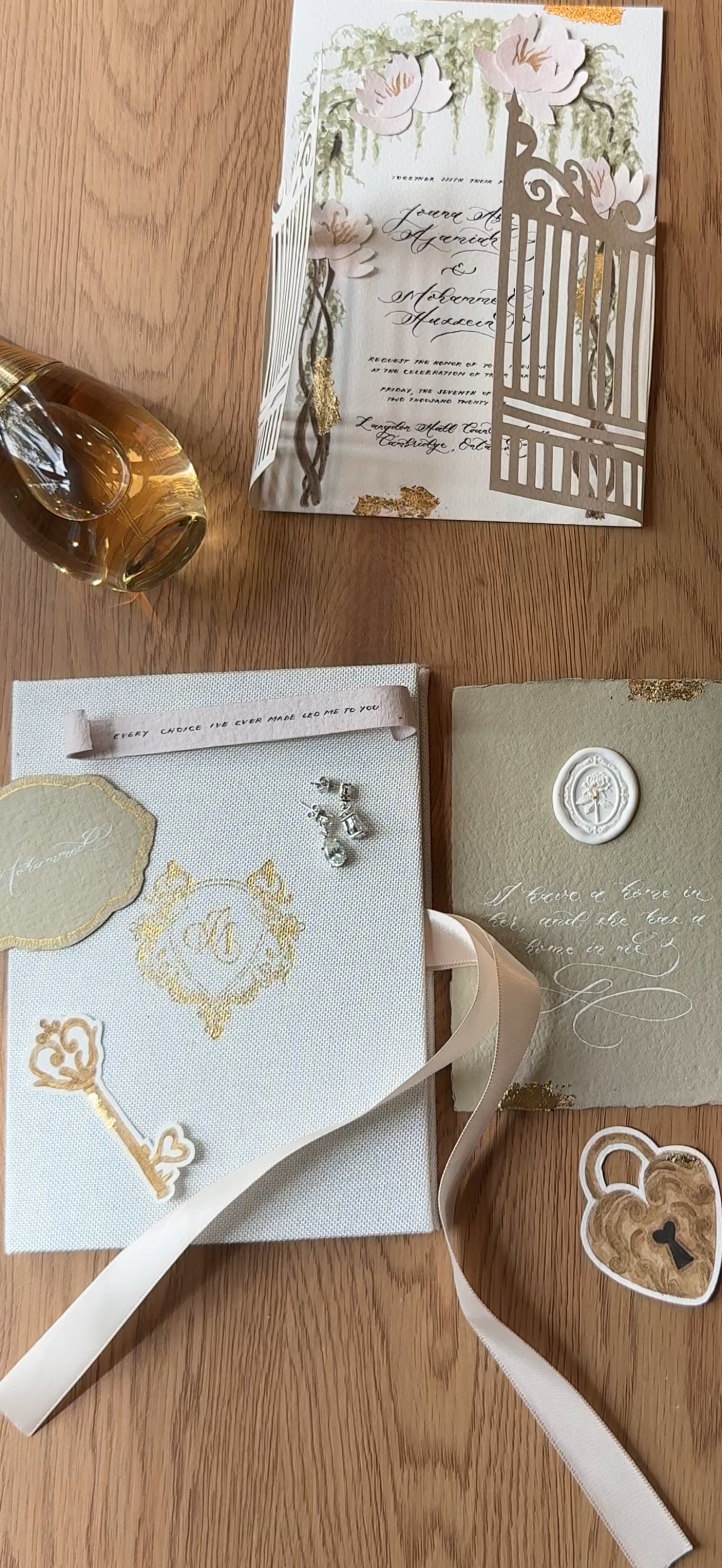 Invitation card with floral design and gold accents, small jewelry pieces, a ribbon, and a message card with gold decorative designs on a wooden surface.