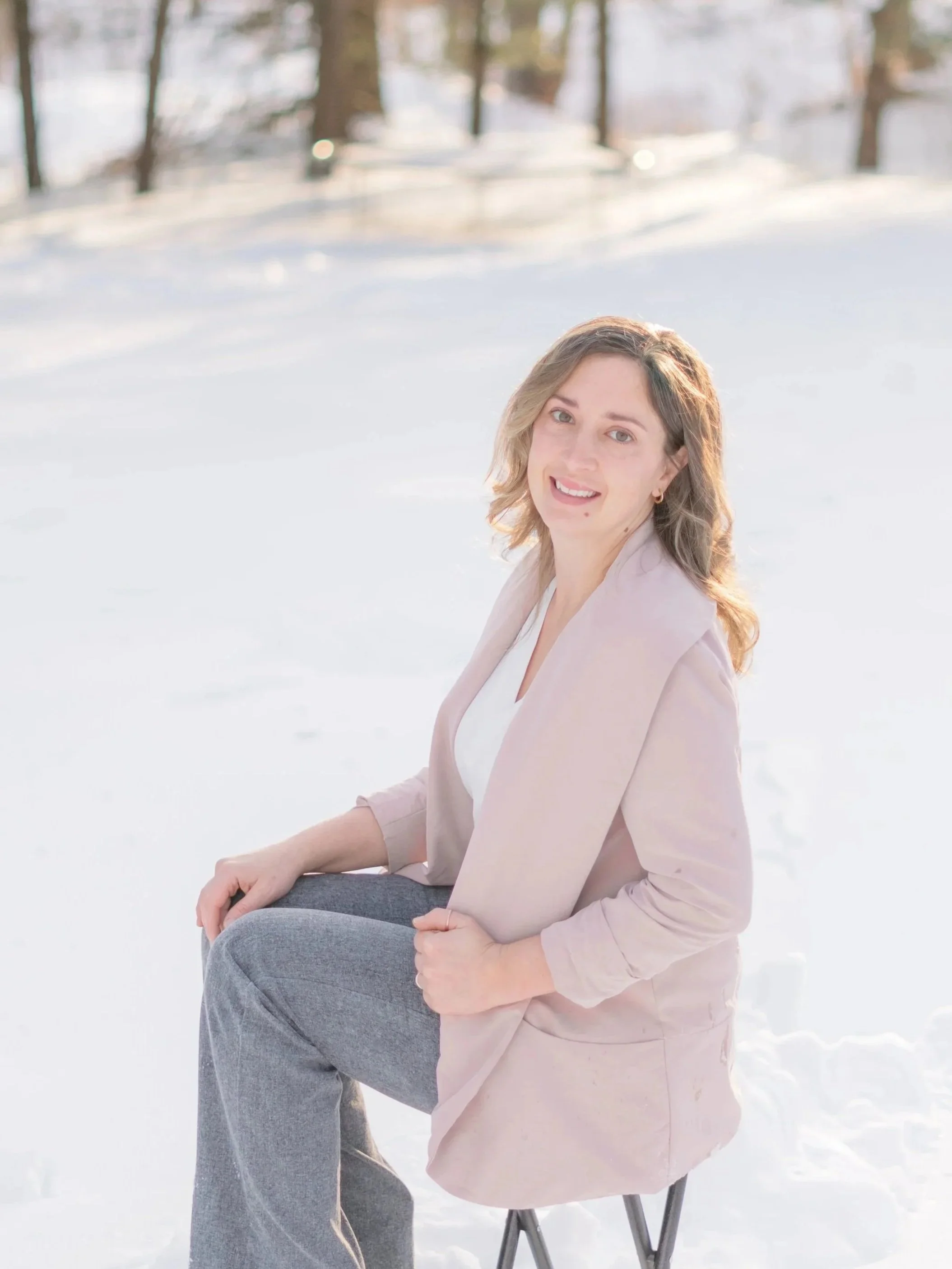 Portrait of photographer sitting on a chair outdoors in snowy landscape, smiling, with trees in the background.