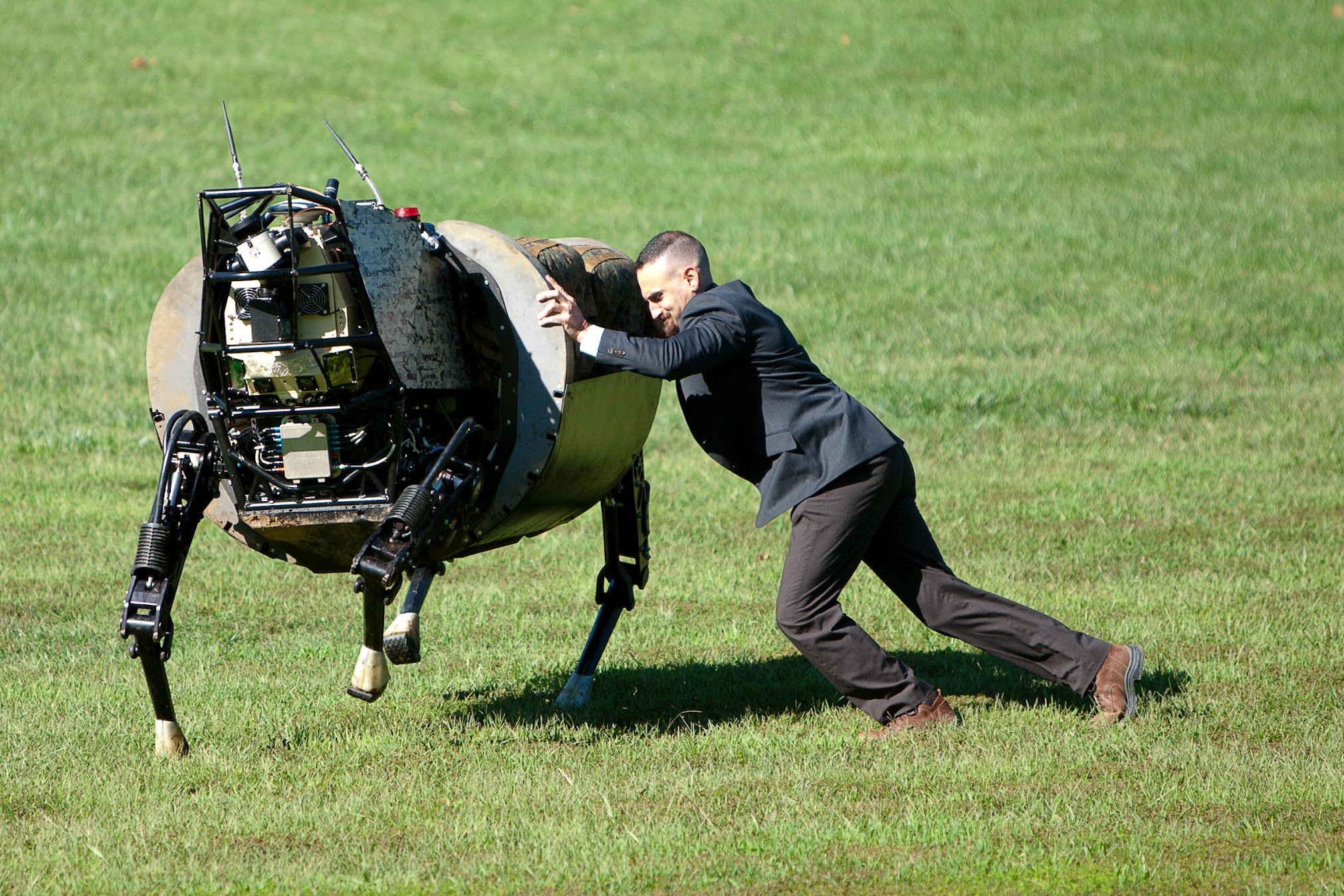 A man in a business suit pushes against a lunar lander model on a grassy field.