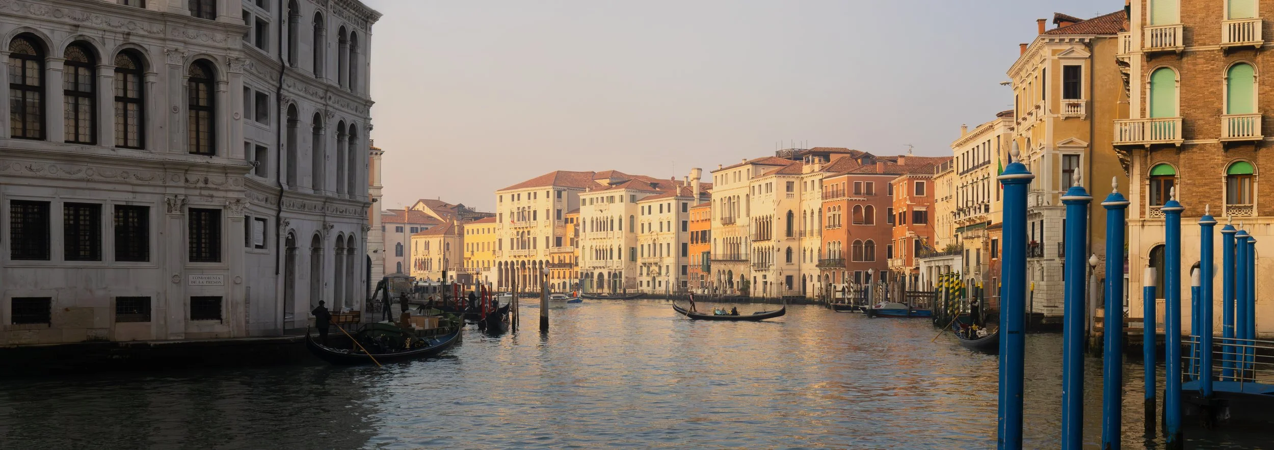 View of a canal in Venice, Italy, with gondolas and historic buildings lining the waterway during sunset.