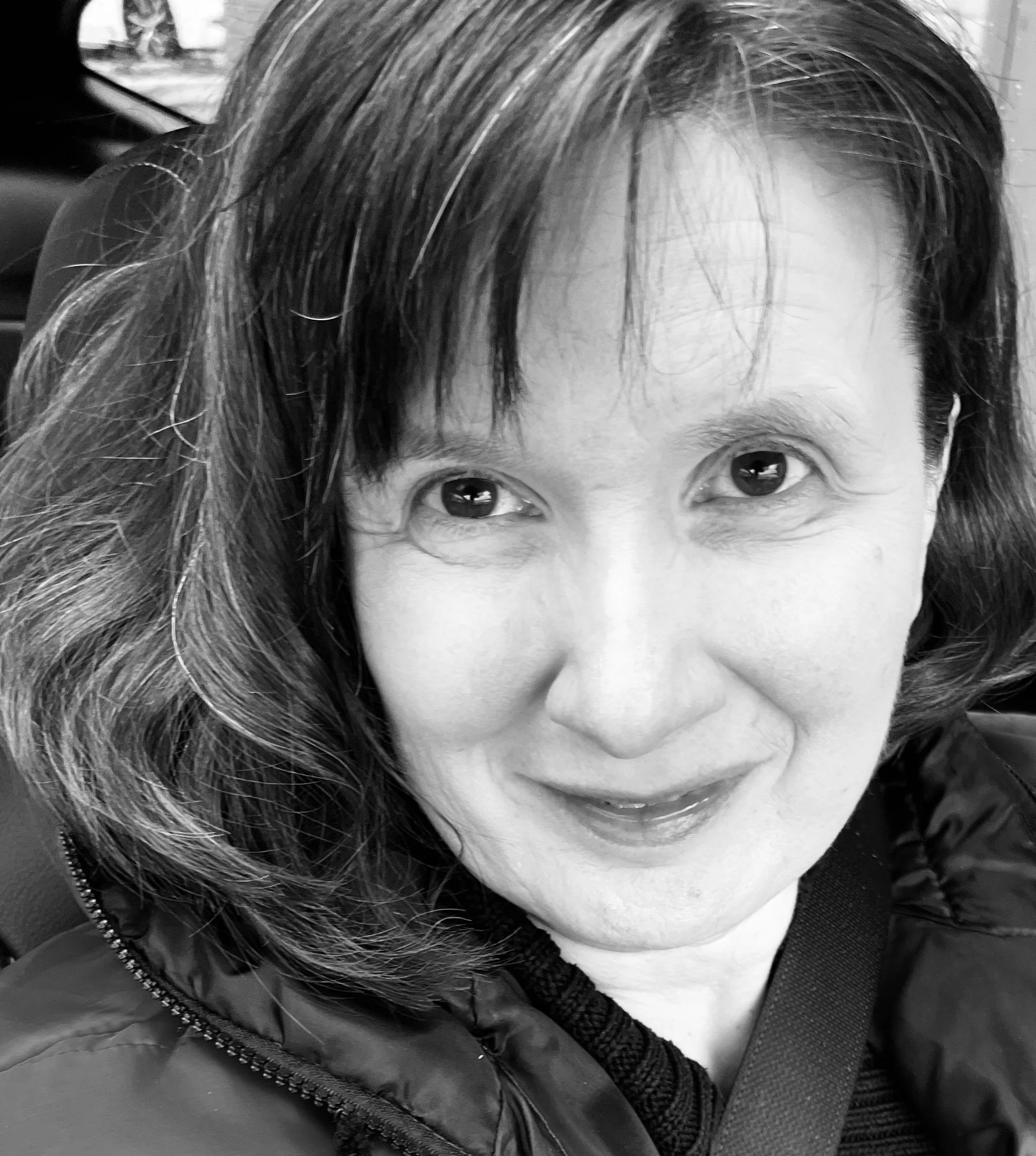 The therapist-A smiling woman with shoulder-length hair, wearing a dark jacket, sitting in a car.