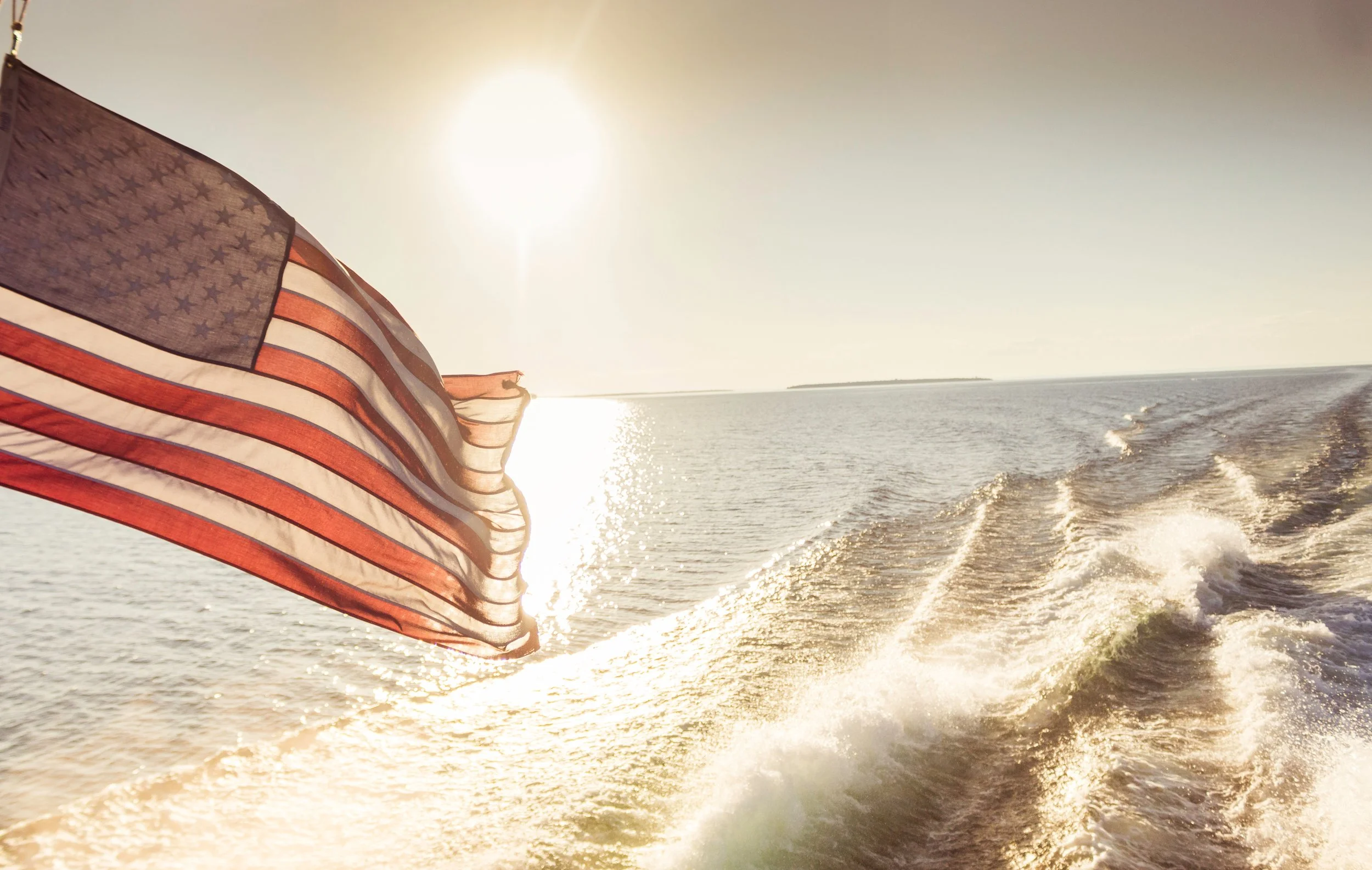 American flag flying on a boat or watercraft as it speeds through the water during sunset or sunrise.