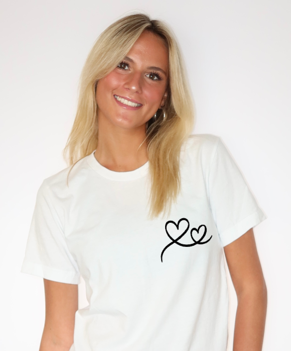 A young woman with blonde hair, wearing a white t-shirt with a black heart drawing and smiling, against a plain white background.