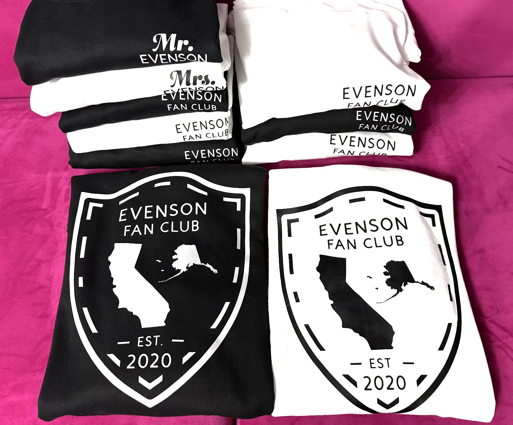 Stacked black and white t-shirts and poster prints with 'Evenson Fan Club' logo, featuring a California map and the year 2020, on a pink surface.