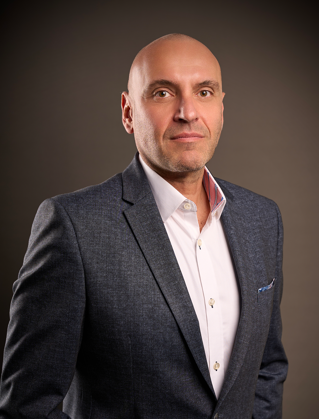 Portrait of Daniel Atanasovski in a dark blazer and white shirt, standing against a neutral background, looking directly at the camera.