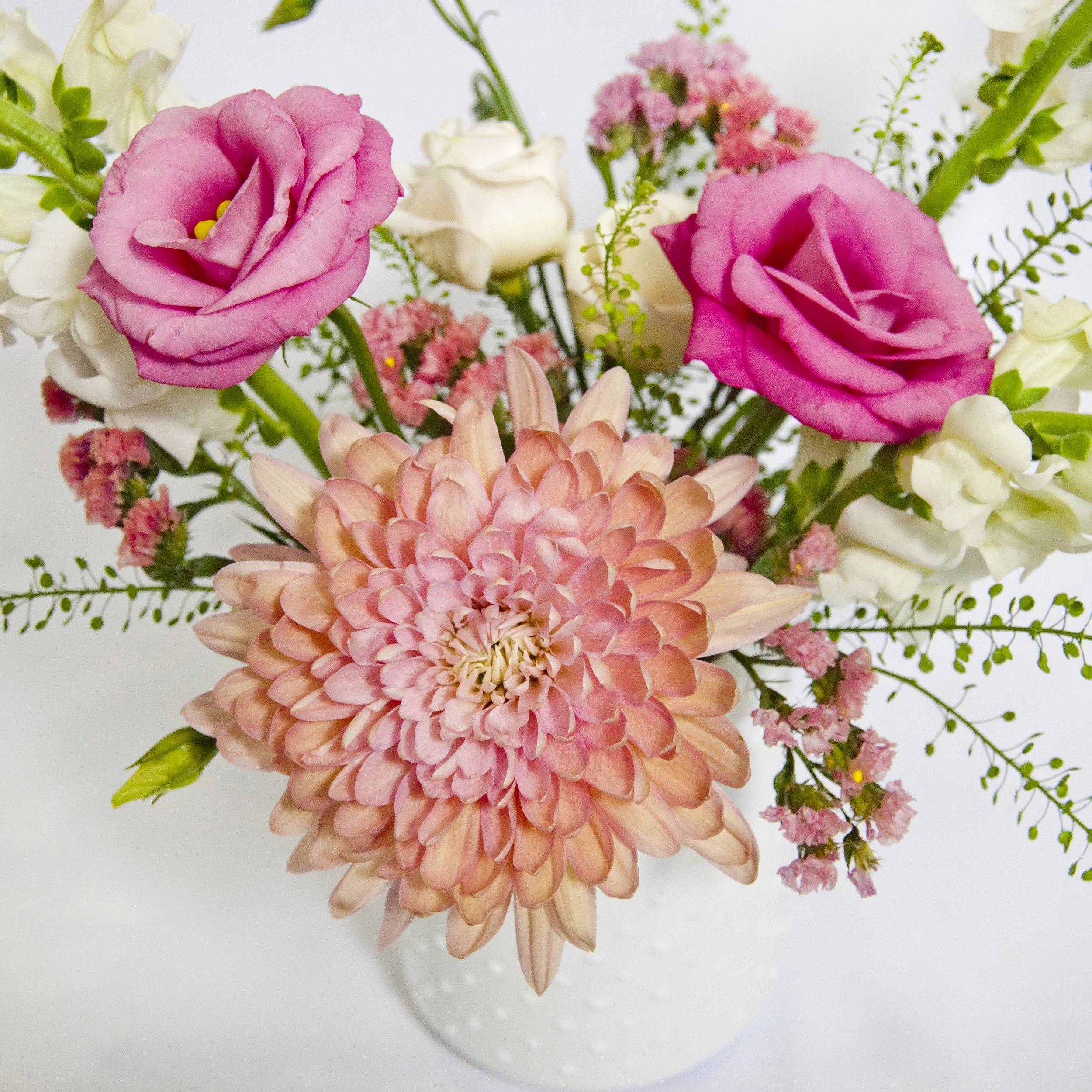 Example arrangement for the Floral Design Workshop with Zeeland Recreation. Close-up of a bouquet of pink, peach, white, and green flowers on a white background.