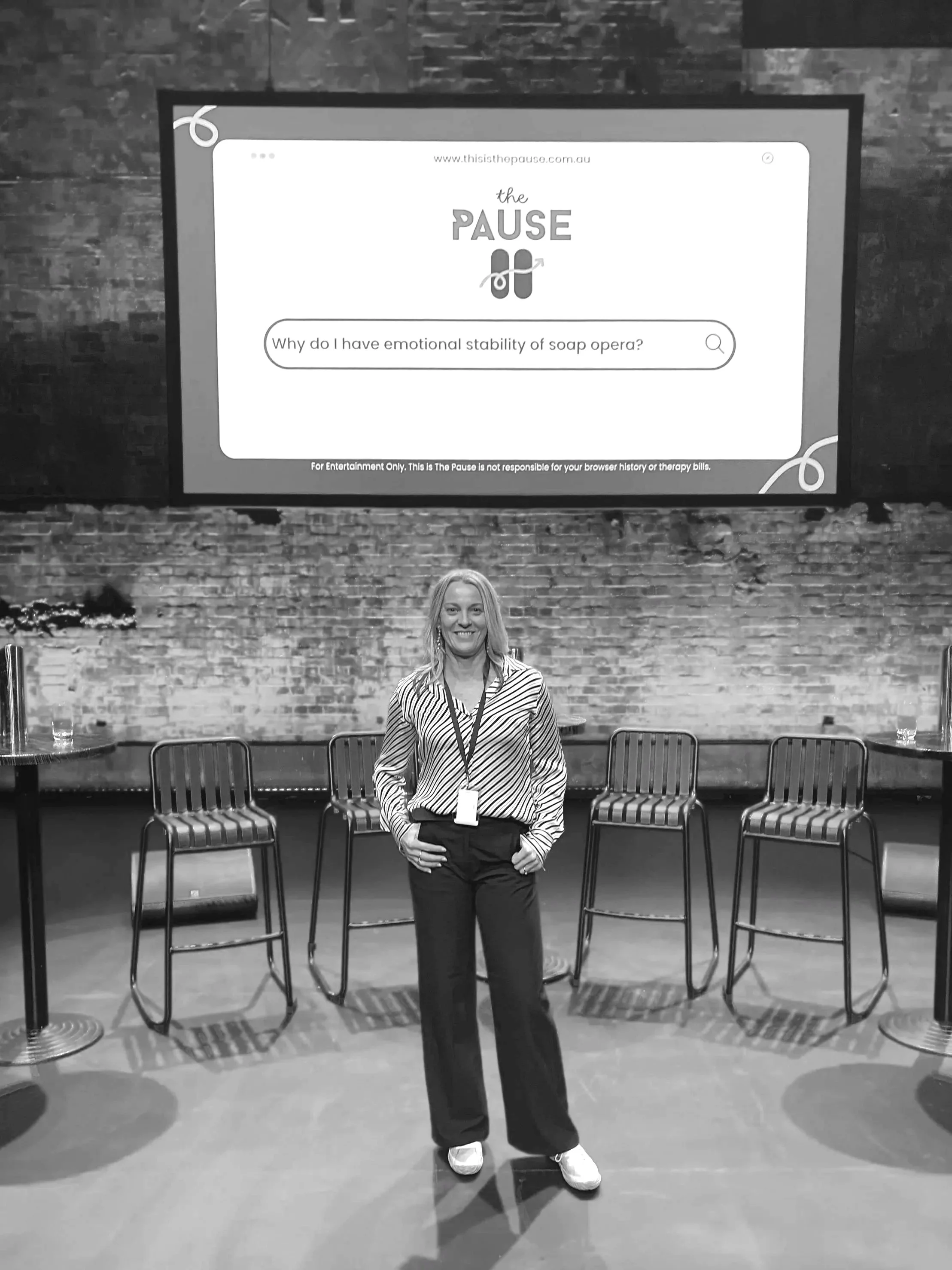 A woman standing in a presentation area with a large screen behind her displaying a website for 'The Pause' with a question about soap opera emotional stability.