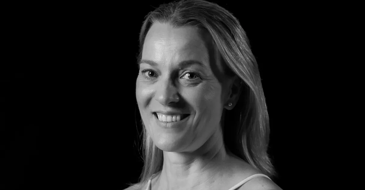 Black and white portrait of a smiling woman with shoulder-length hair, wearing a sleeveless top, against a dark background.