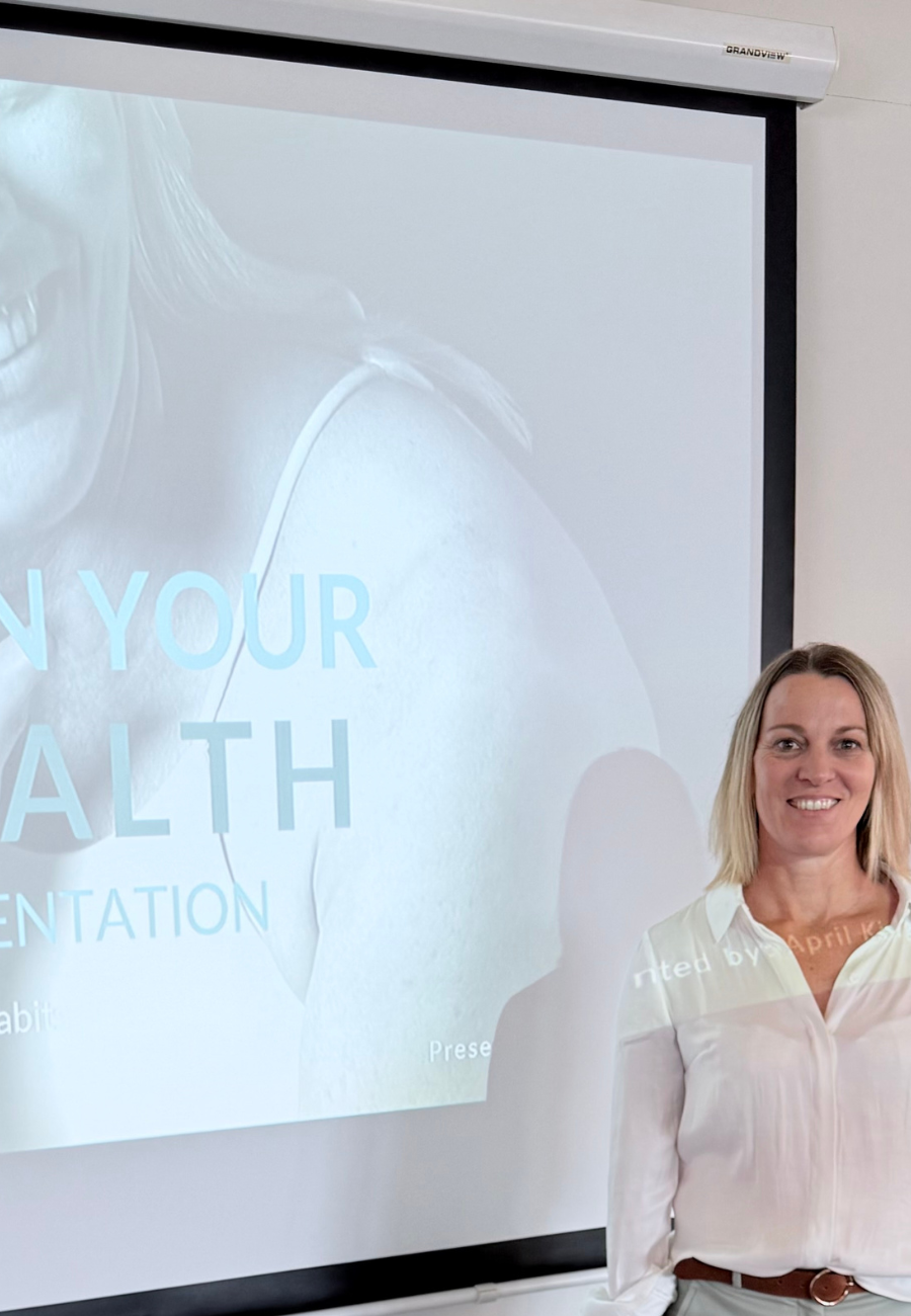 A woman standing in front of a projection screen with the title 'Enhancing Your Health Presentation' and a close-up of a woman smiling on the slide.