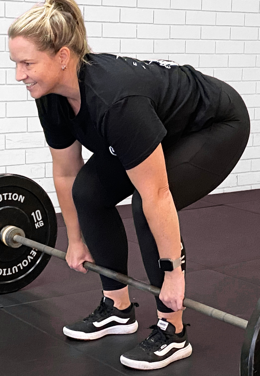 A woman in athletic clothing performing a deadlift exercise with a barbell in a gym.