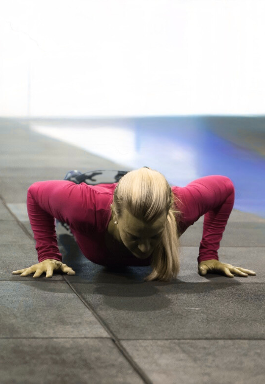 Woman in pink workout top performing push-up on gym floor.