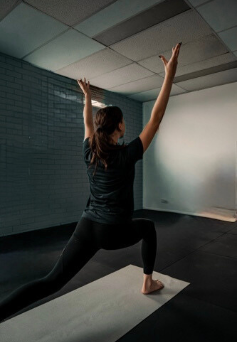A woman practicing yoga in a studio, performing a lunge with arms raised overhead.