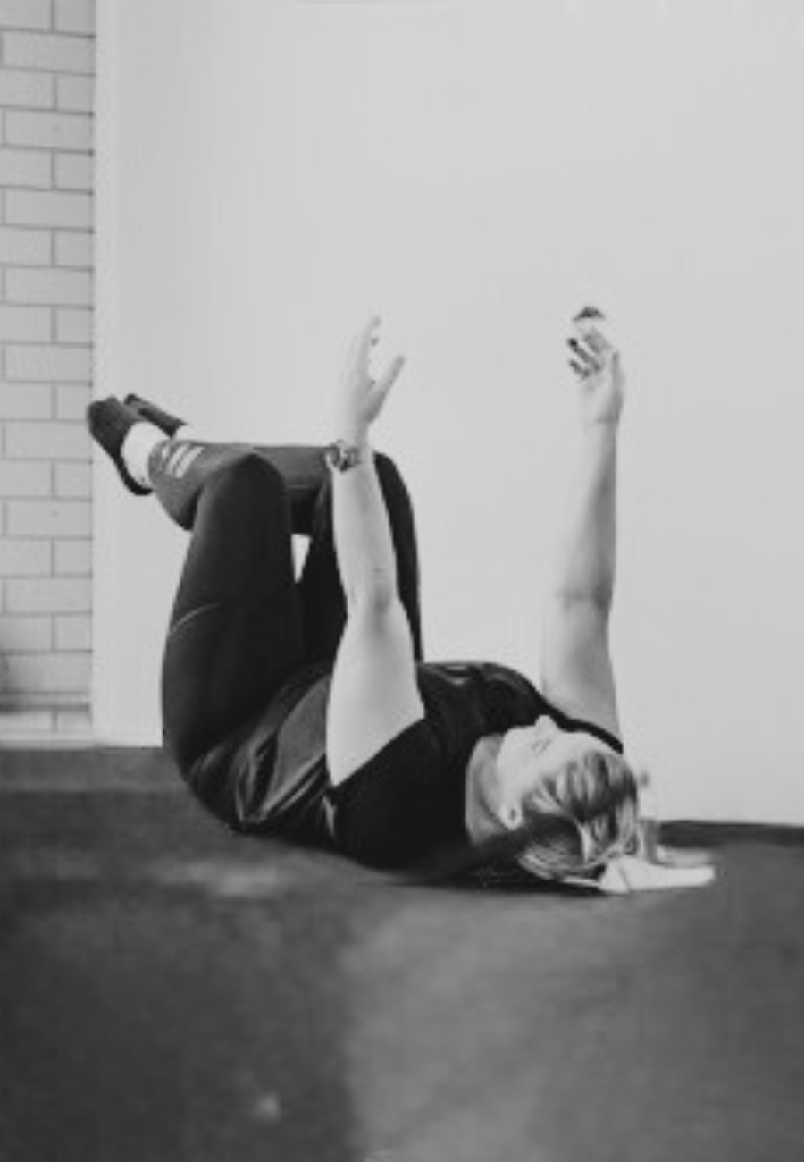A woman lying on her back on the floor, doing an exercise. She is wearing athletic clothing.