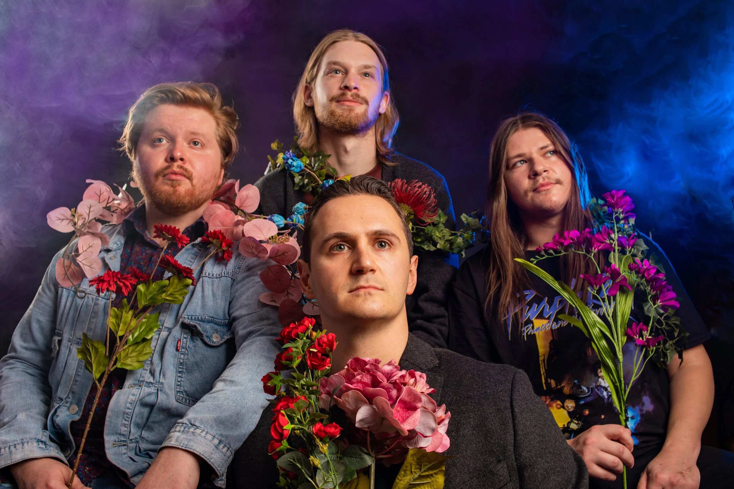Five people seated with colorful flowers, dark background with purple and blue lighting.