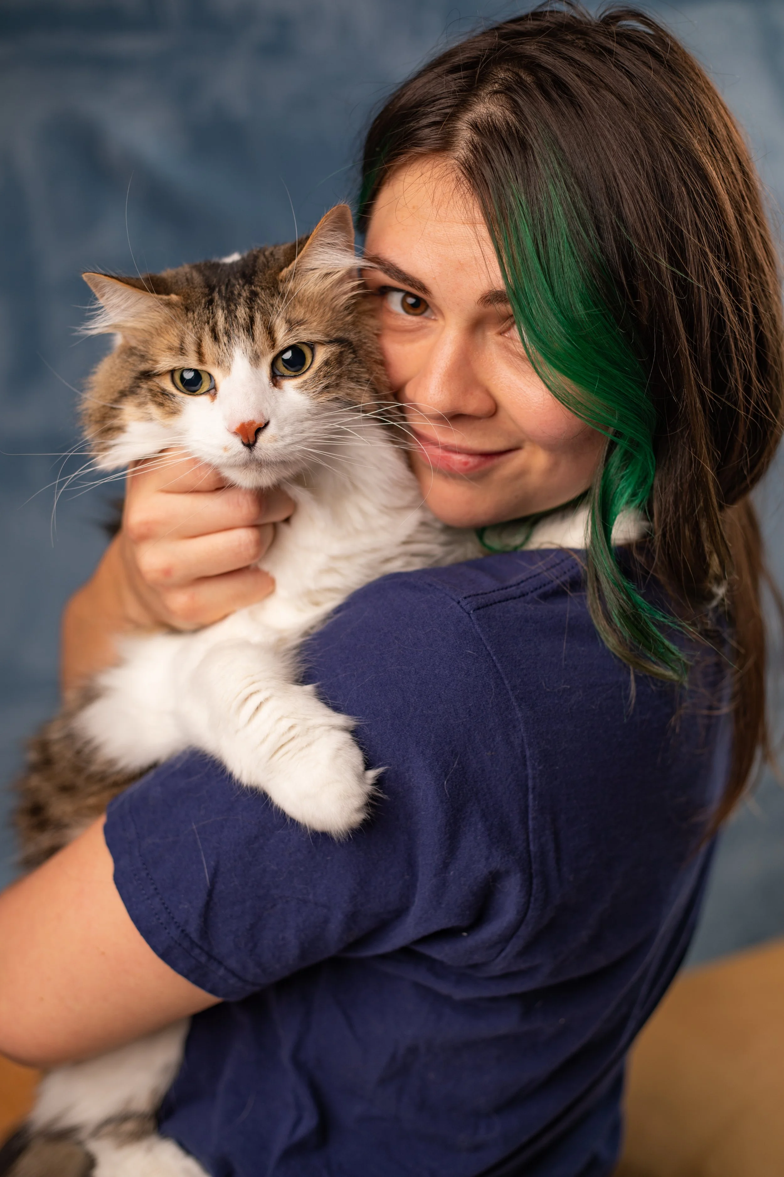 A woman with brown hair and green highlights holding a fluffy cat with white and tabby fur, both looking at the camera.