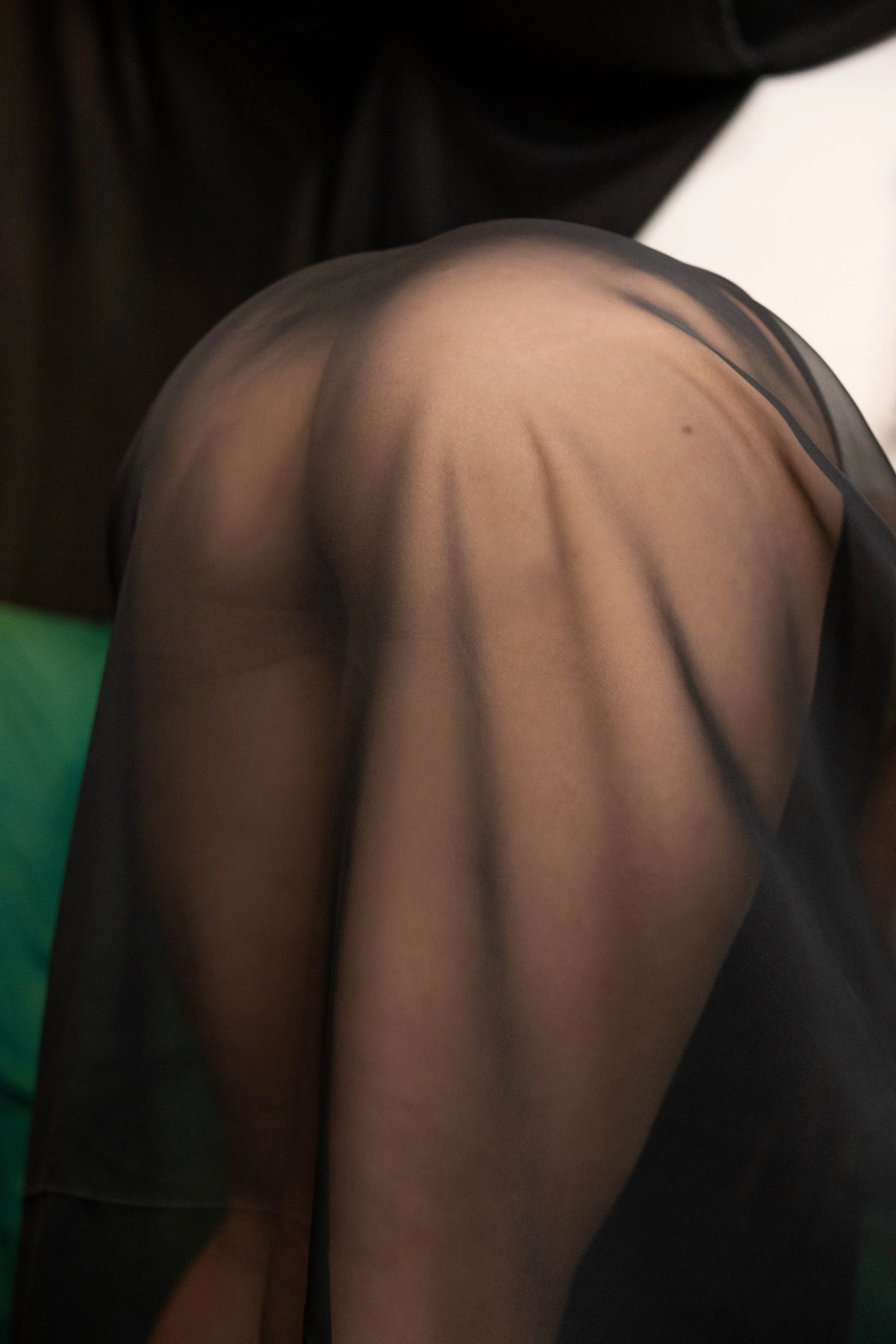 Close-up of a person wearing black sheer tights, with a focus on the upper thigh and shoulder area.