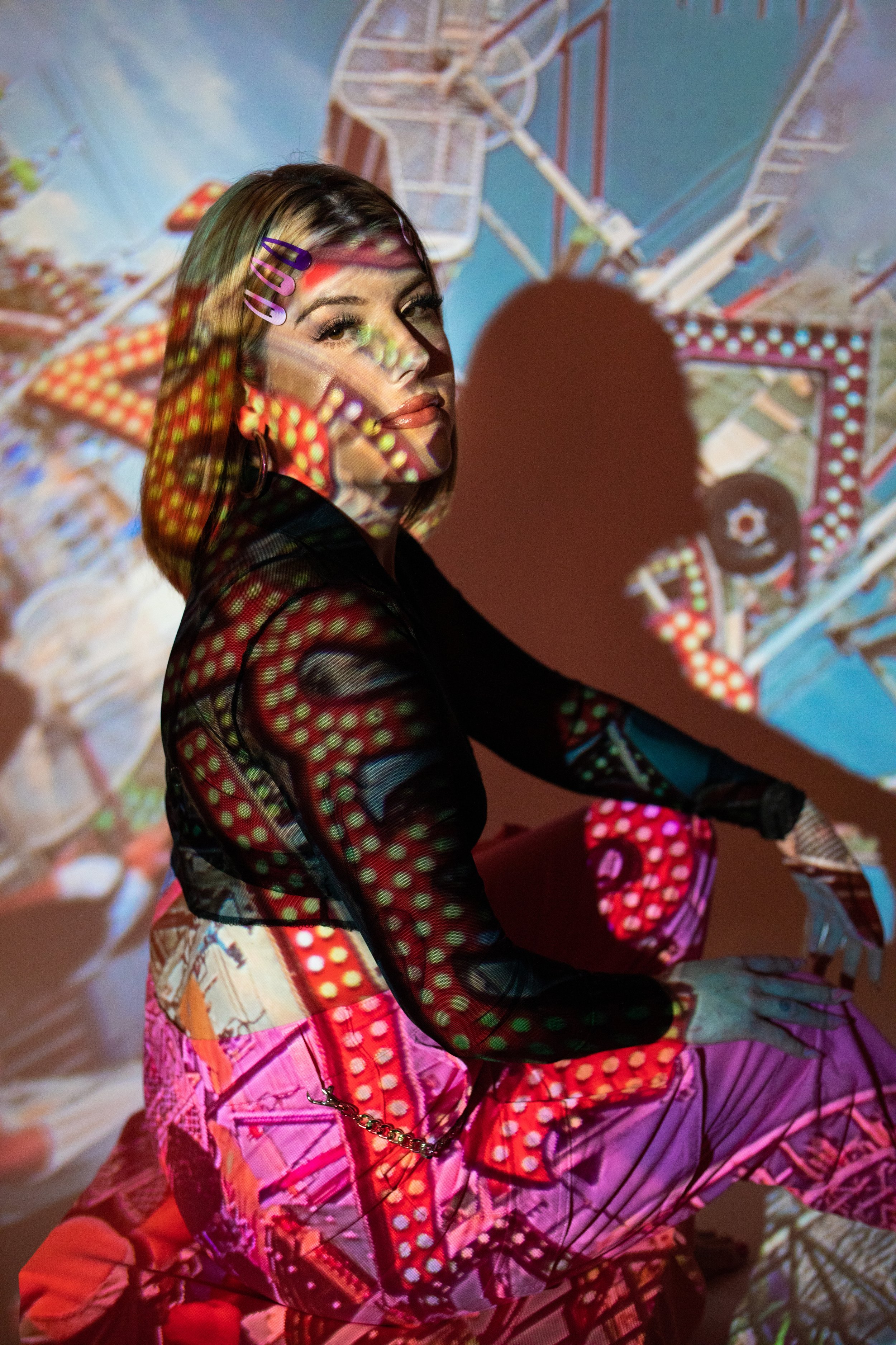 A woman sitting against a wall with colorful, patterned light projections on her and her surroundings.