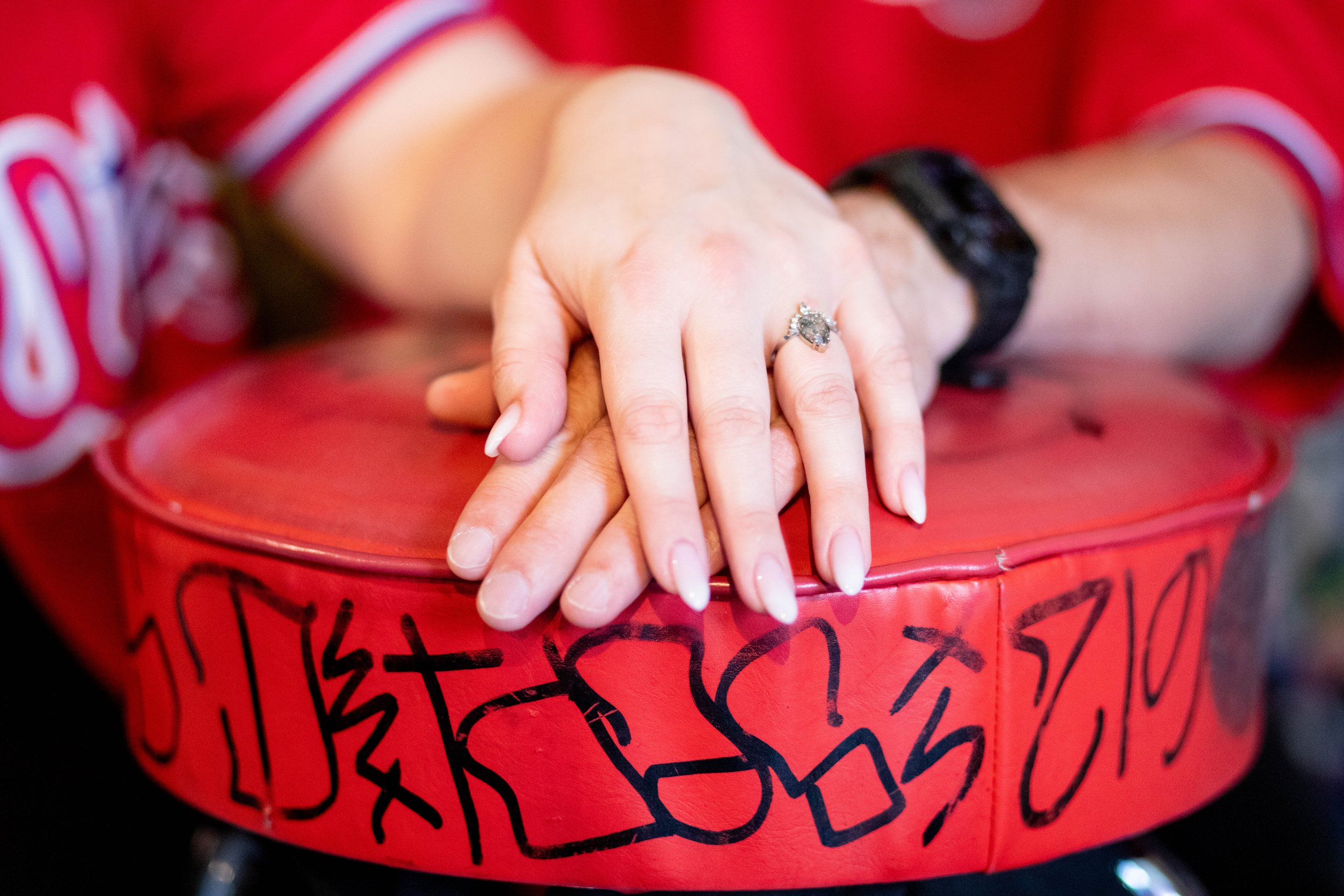 Close-up of a woman’s hands with a large engagement ring, resting on a red graffiti-covered surface.