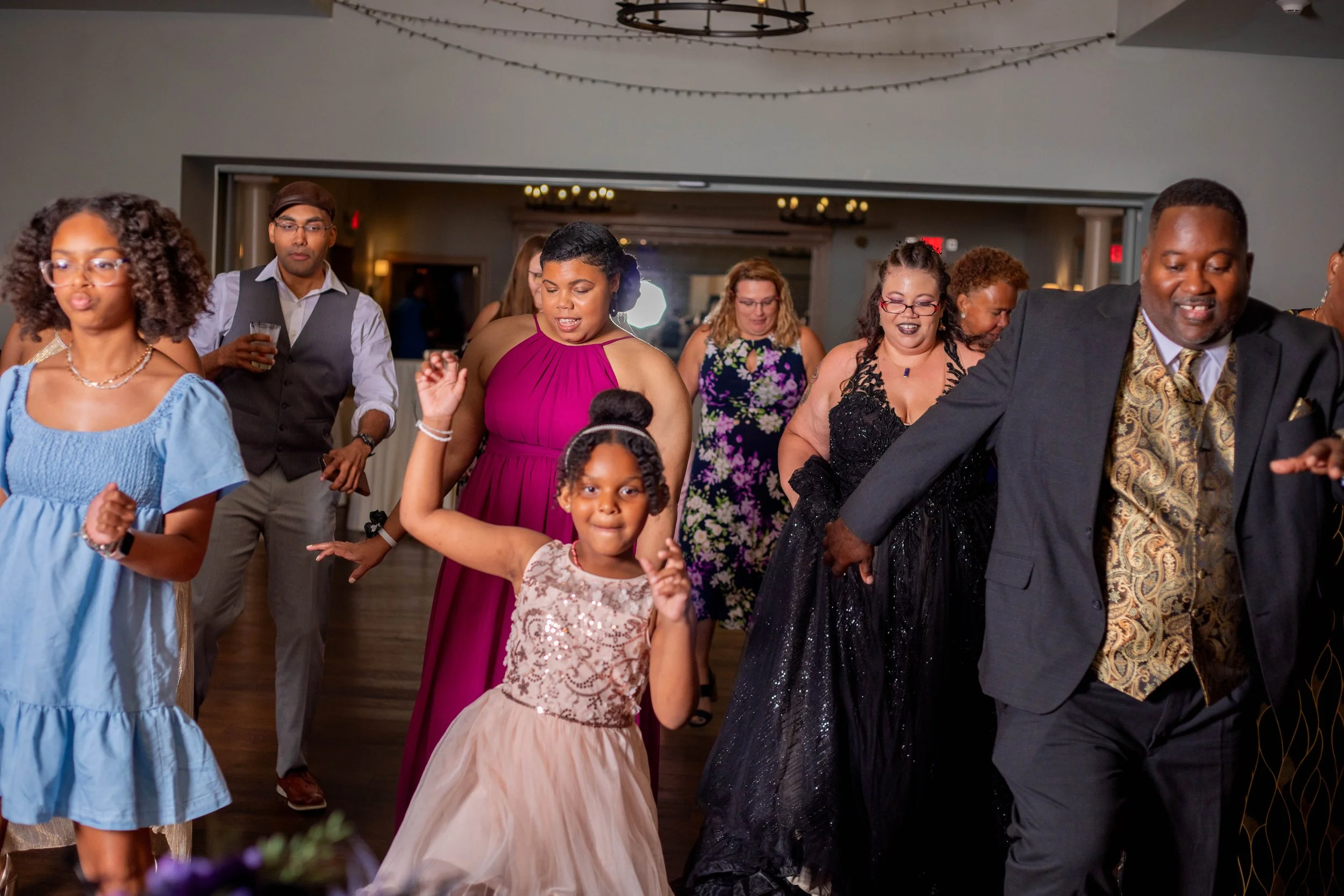 People dancing at a celebration event, including women, men, and children in formal and semi-formal attire.