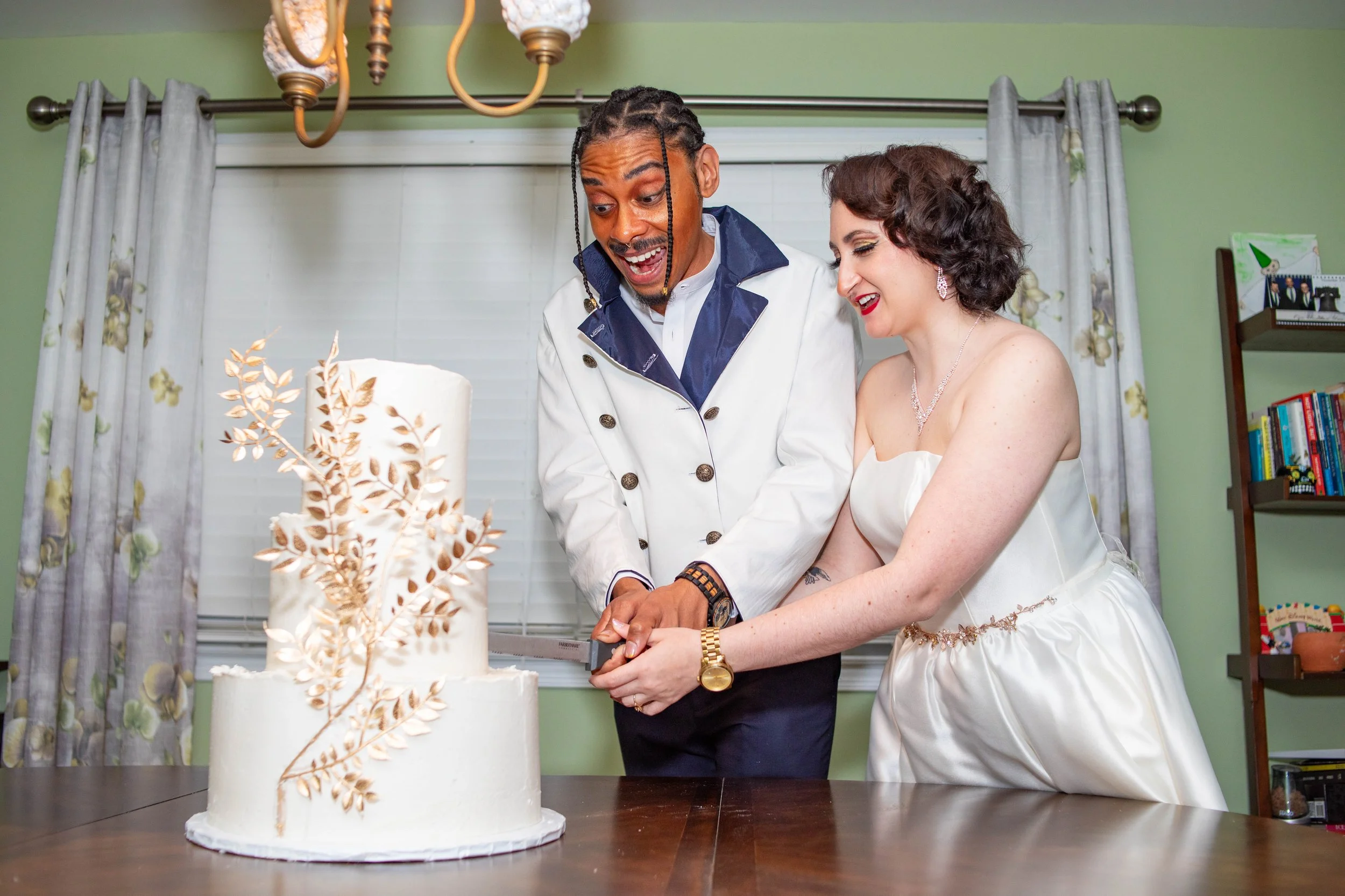 A bride and groom cutting a wedding cake together during their wedding reception, with both showing joyful expressions.