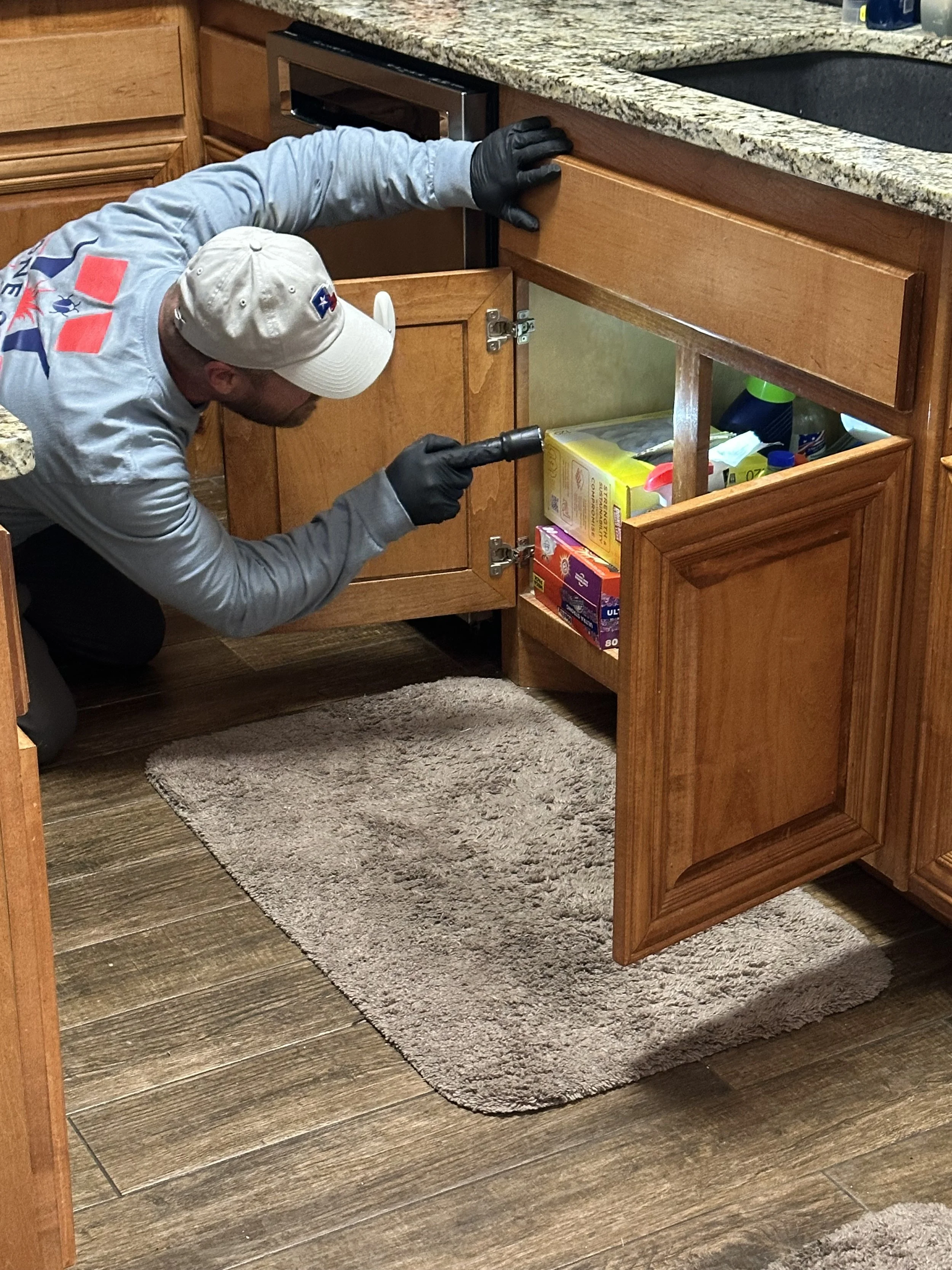Pest control technician inspecting a kitchen cabinet during a residential pest control service in Fort Worth, Texas.