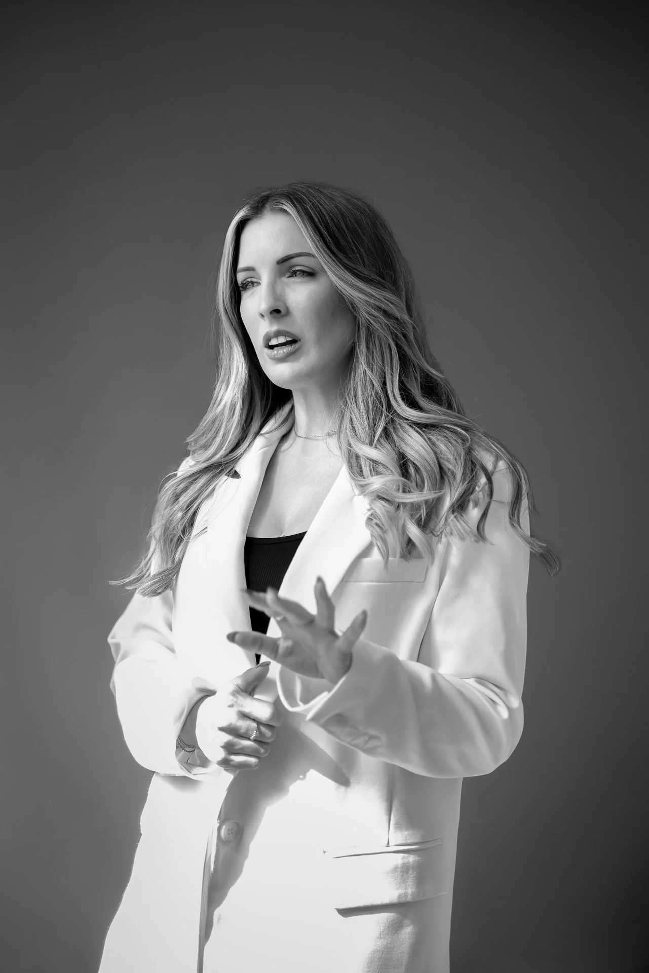 Black-and-white portrait of a woman in a white blazer gesturing while speaking
