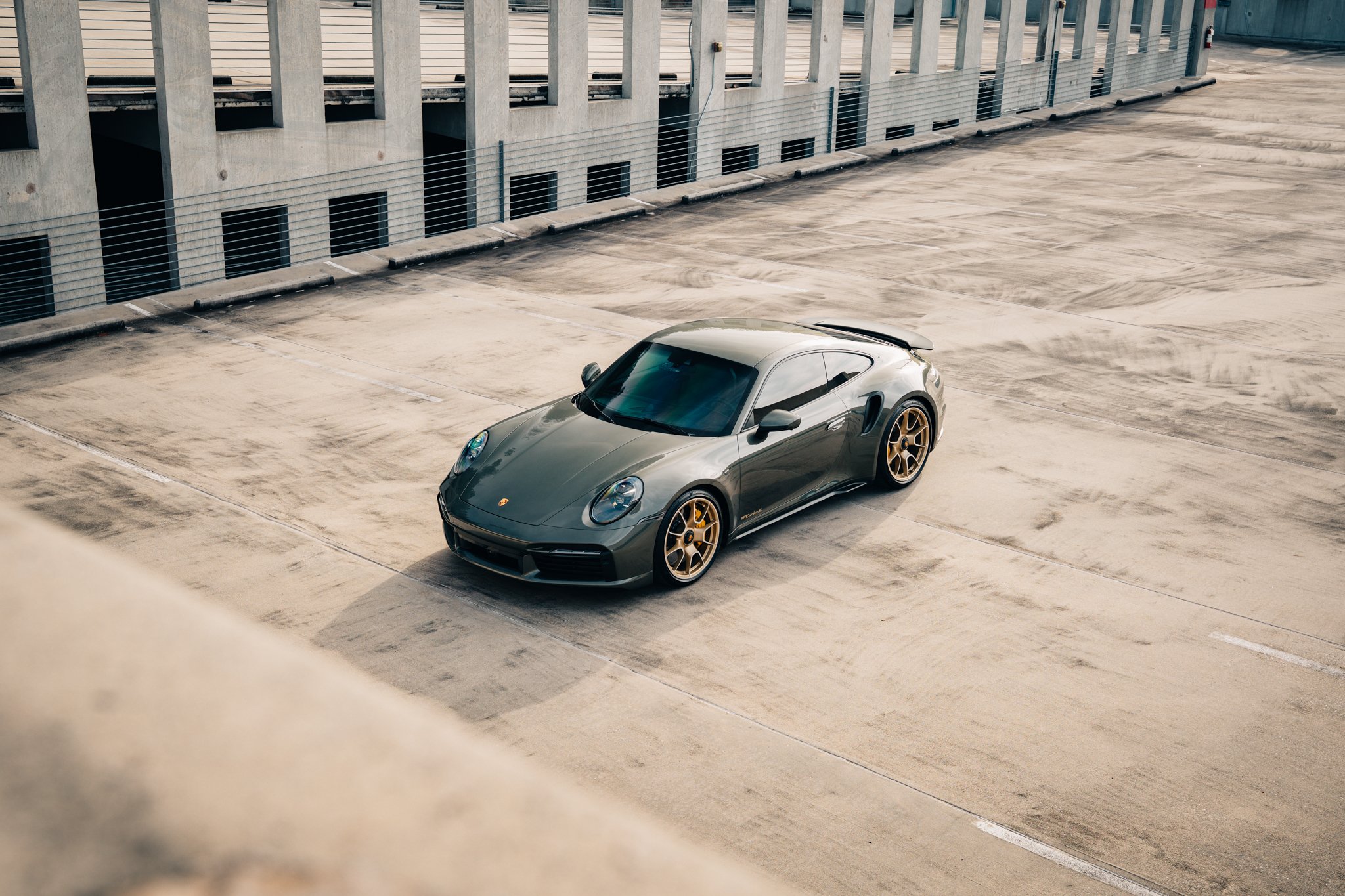 A sleek dark gray sports car with gold rims parked in an empty rooftop parking lot.
