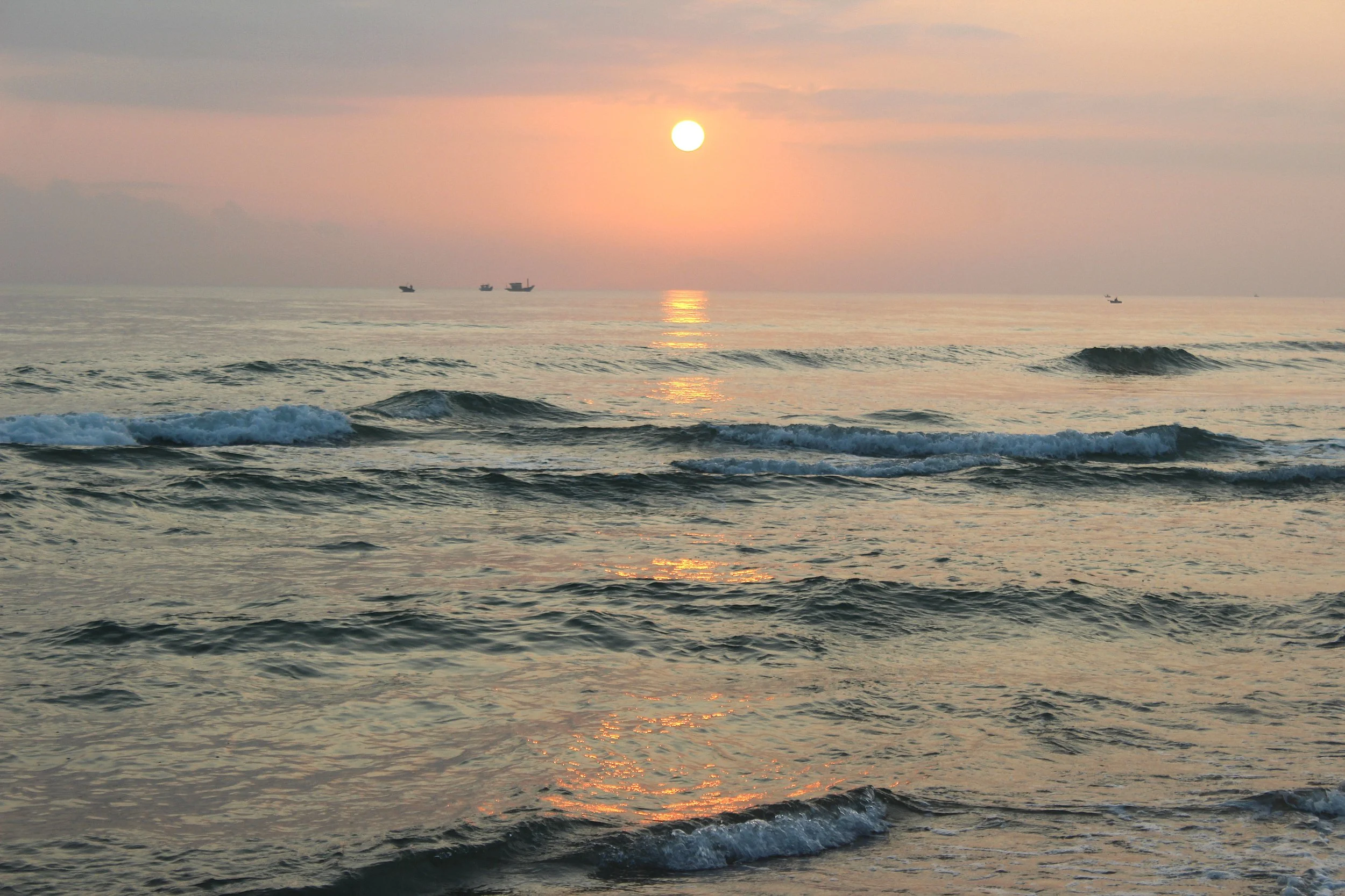 Sunrise over An Bang beach with gentle waves and a few distant boats