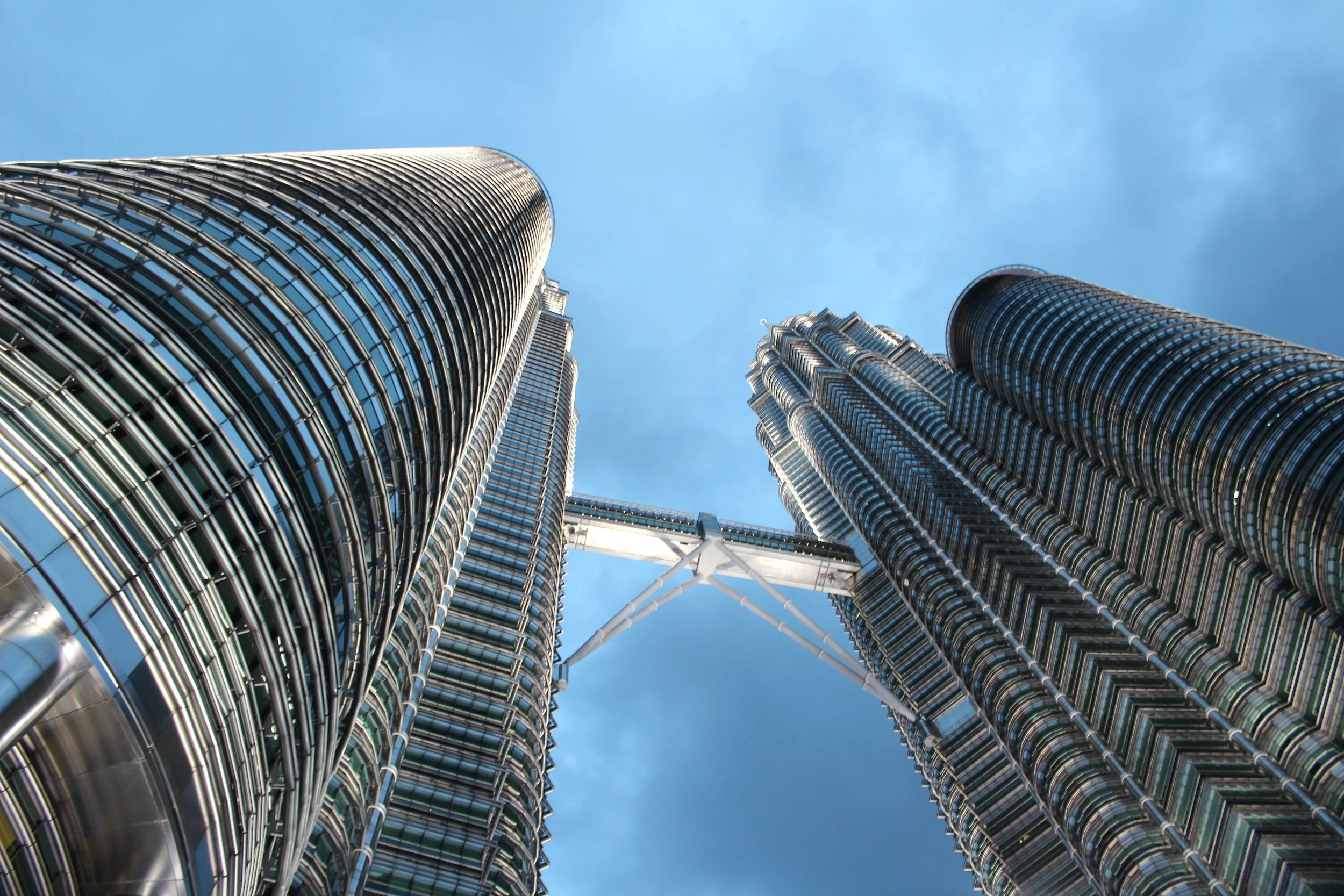 Looking up at the Petronas Towers in Kuala Lumpur, Malaysia, with a clear blue sky in the background.
