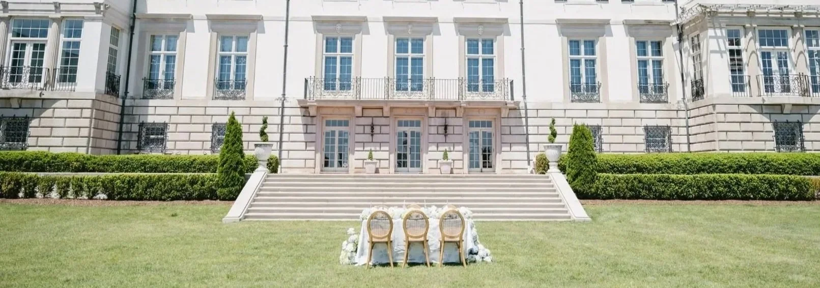 Beautiful white mansion with steps leading up to the entrance and outdoor table with chairs on the lawn, decorated for an event.