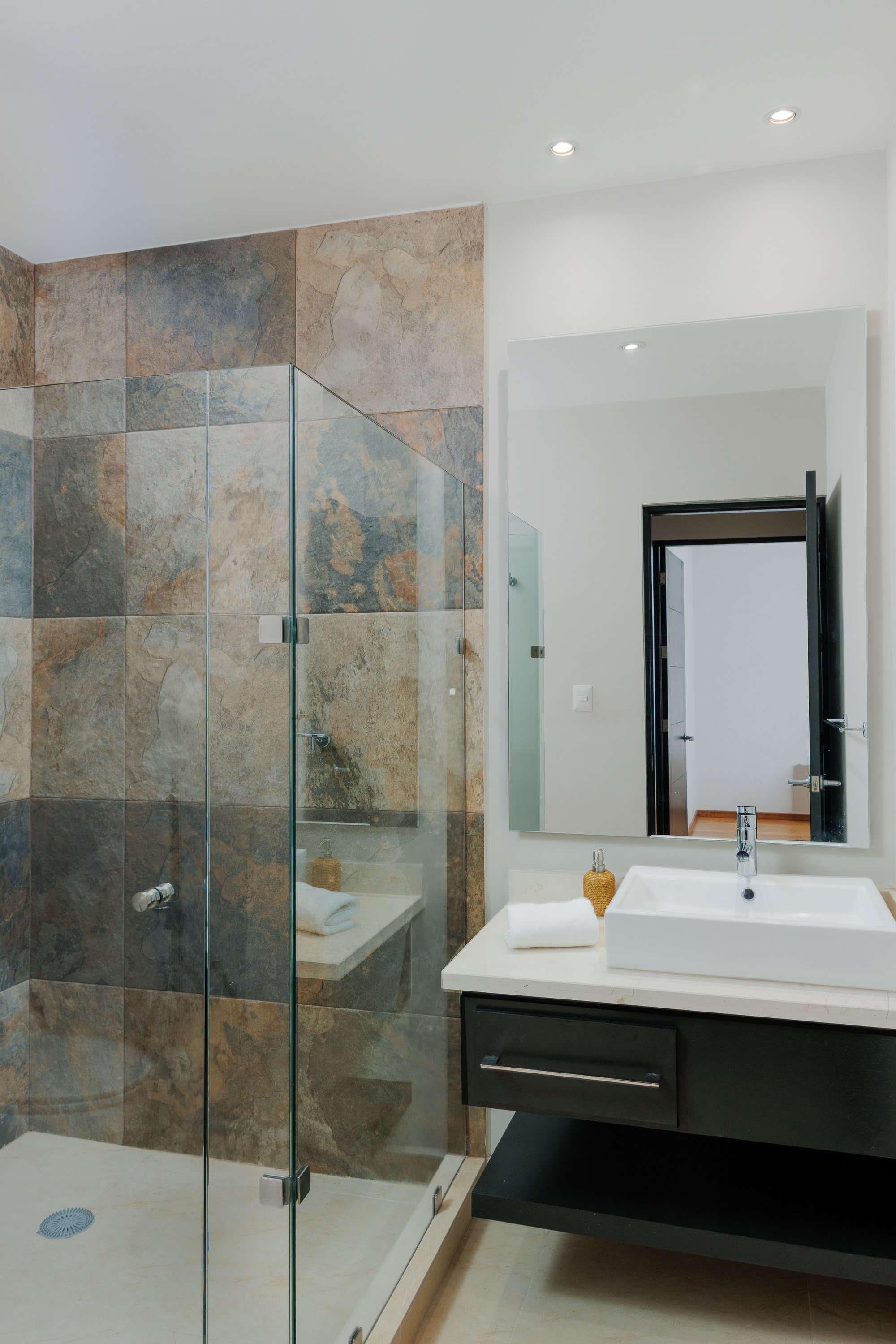 Baño residencial de lujo con acabado pétreo y cancel de vidrio, fotografía de arquitectura interior en proyecto residencial en Querétaro.