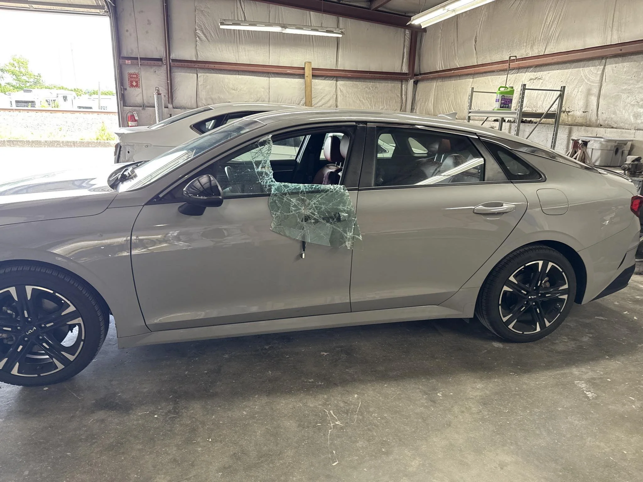 A silver sedan with a shattered front passenger side window in a garage or workshop.