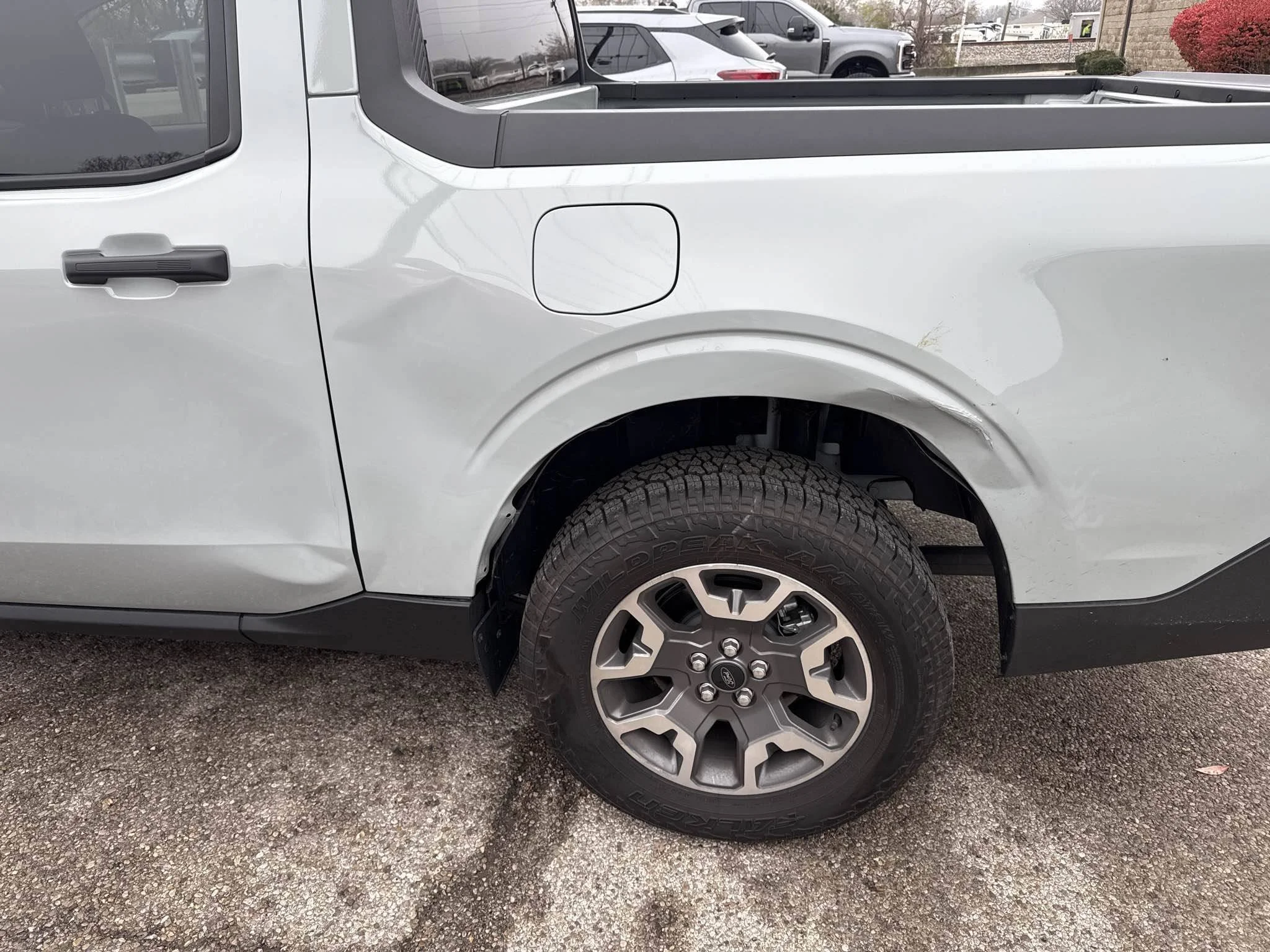 Front passenger side of a grey pickup truck showing the front wheel and part of the truck bed with a black liner.