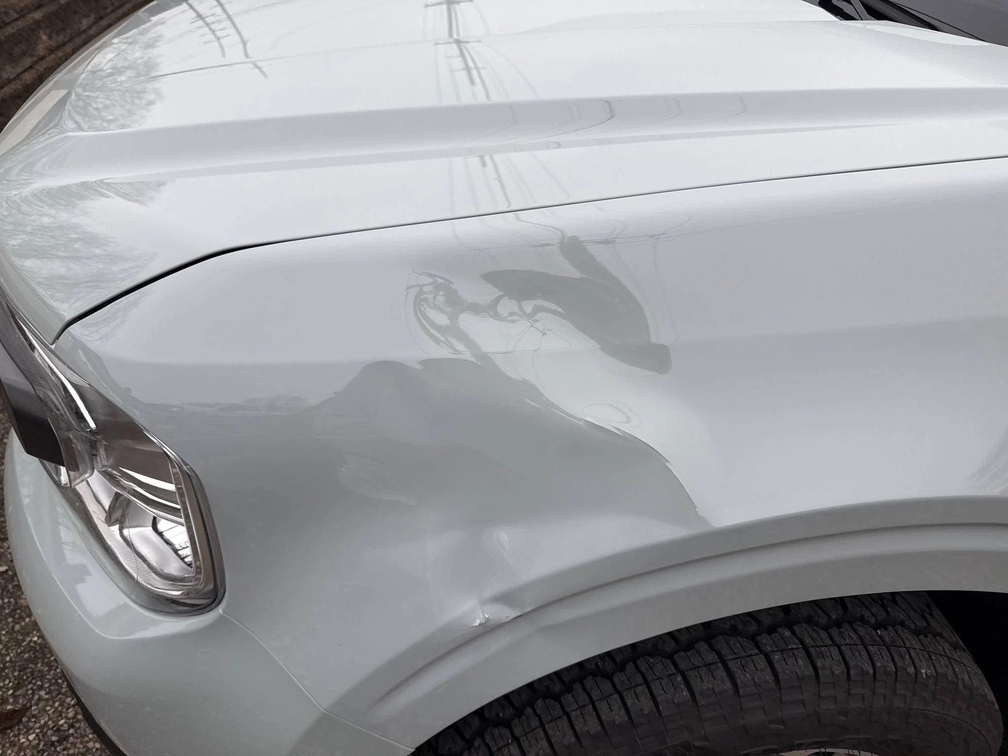 Close-up of a white car with a dented front fender and damage above the wheel.