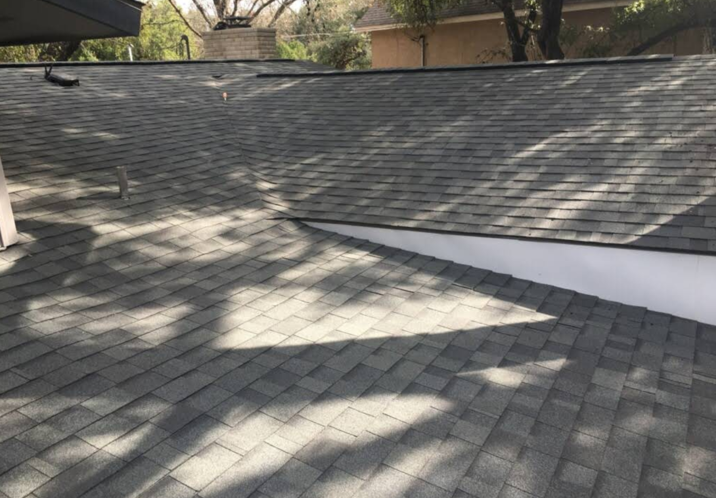 View of a residential shingle roof with shadows cast by nearby trees.