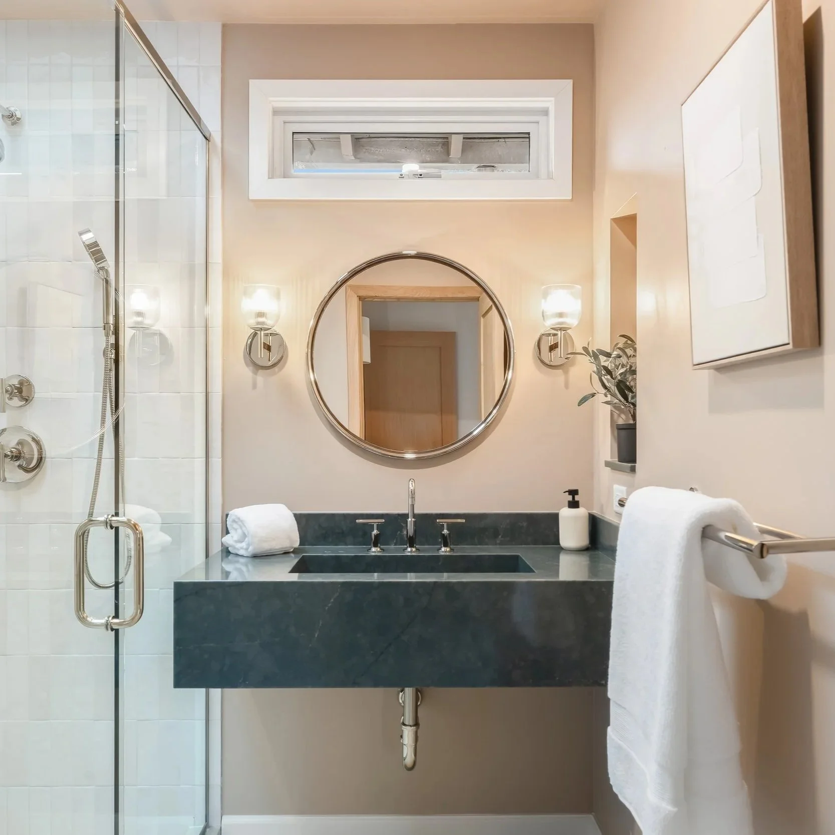 Guest bathroom with soft apricot walls, custom emerald green quartz vanity with integrated sink, and circular mirror with polished nickel sconces.