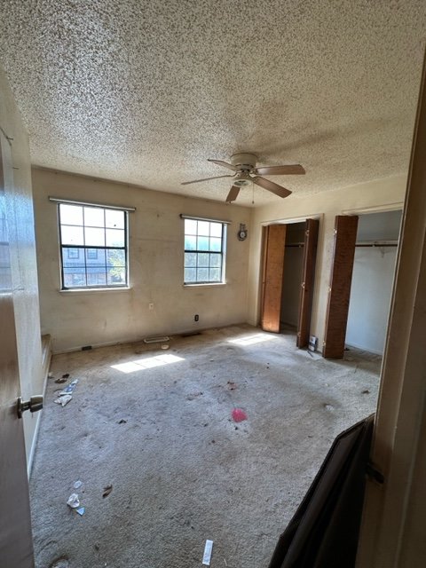 Bedroom before renovation showing original condition with popcorn ceiling and worn carpet.