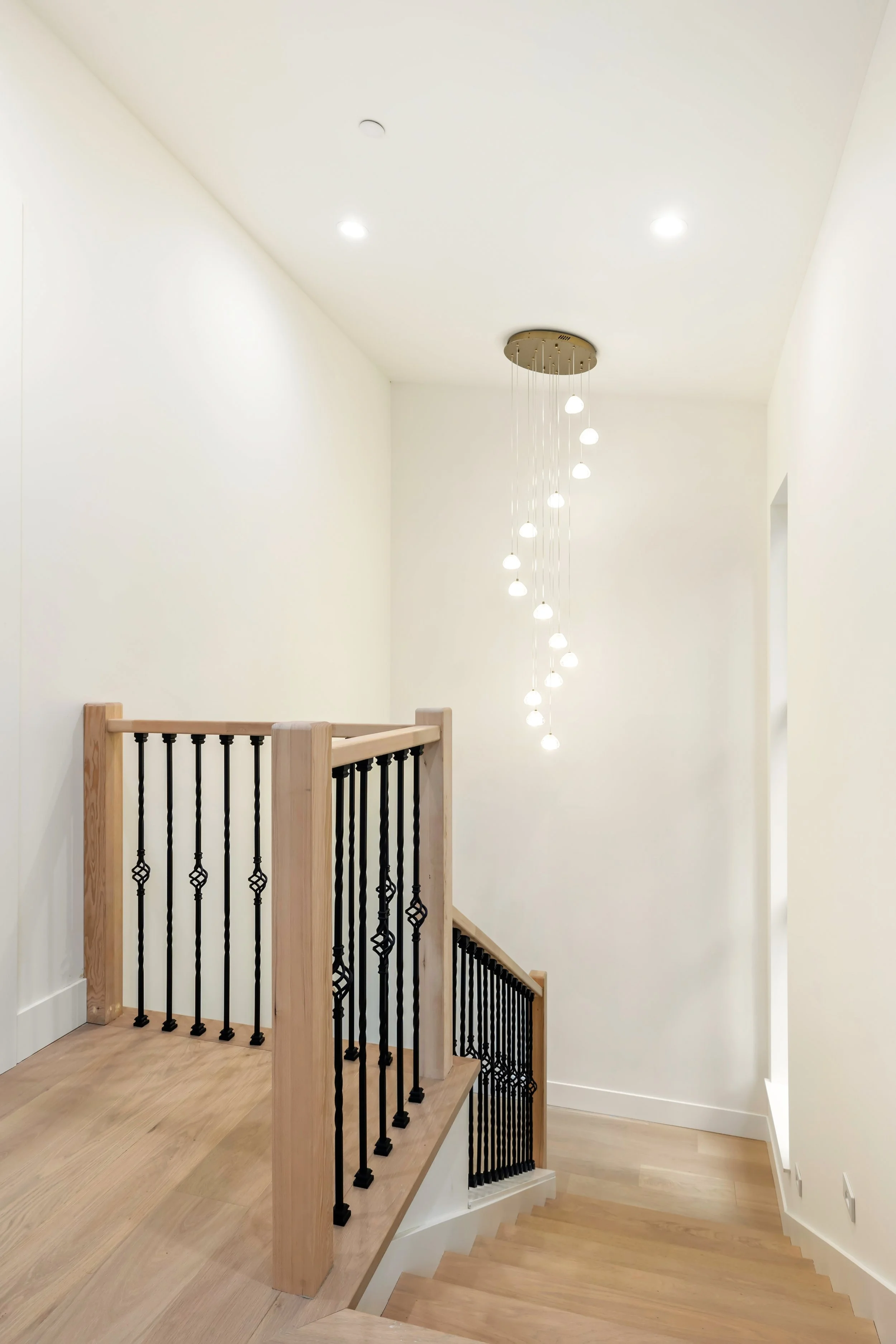 Stairwell with wood railings, black metal balusters and wood treads, with modern brass and glass statement chandelier.